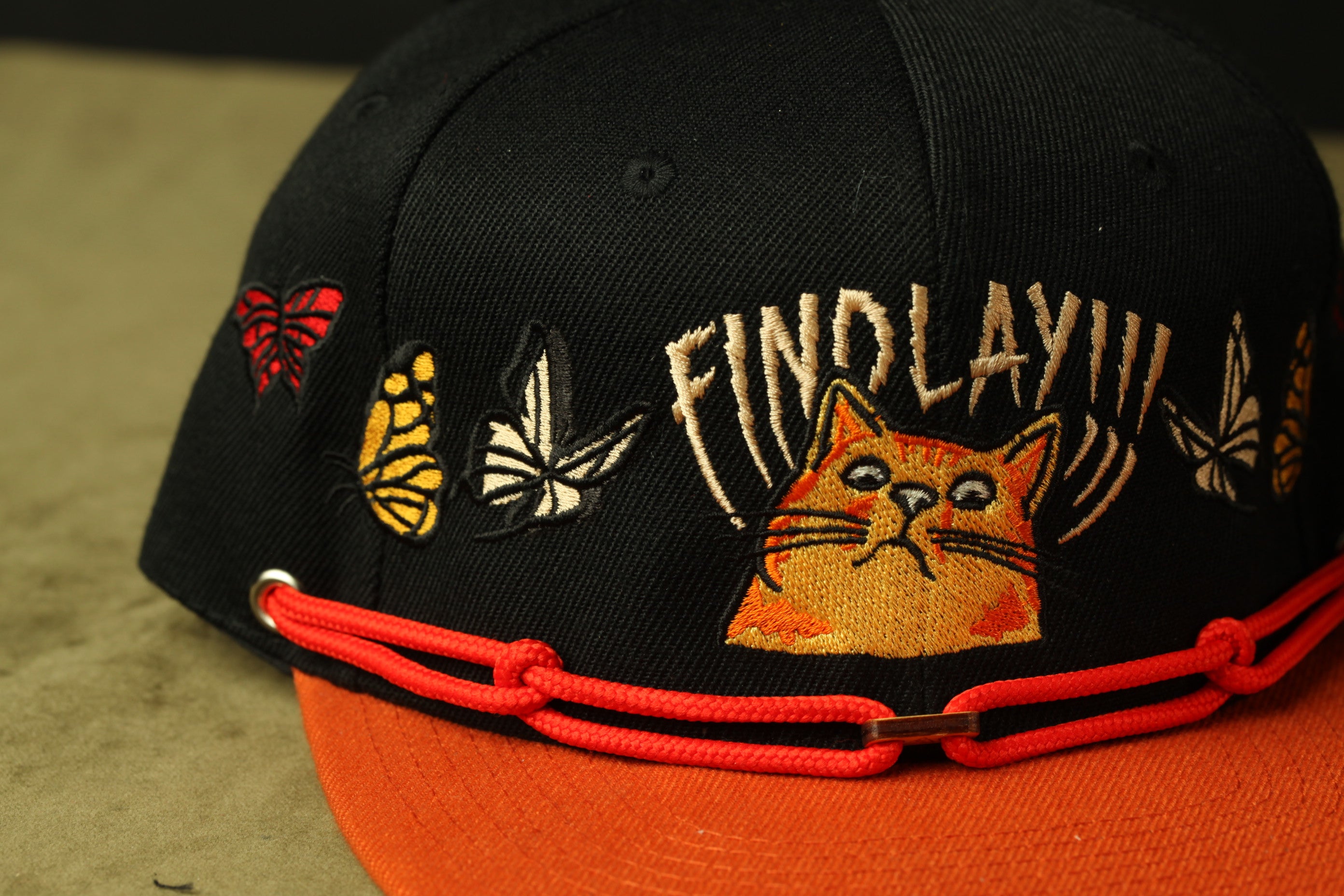 A black baseball cap with a red string and a cat embroidered on it.
