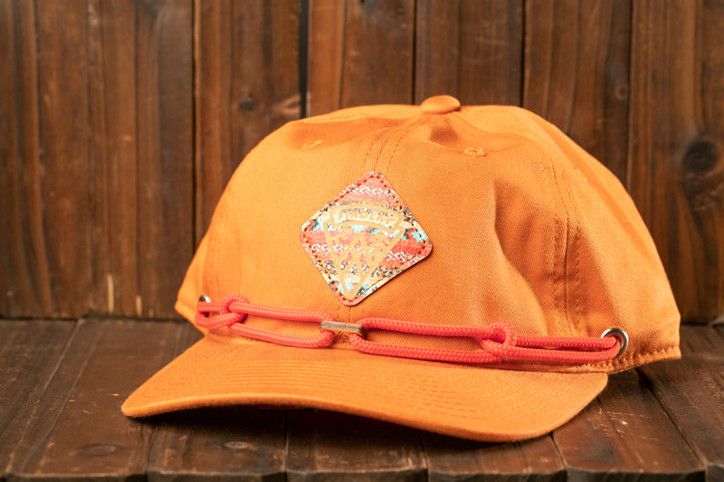 An orange baseball cap with a decorative patch sits on a wooden surface.