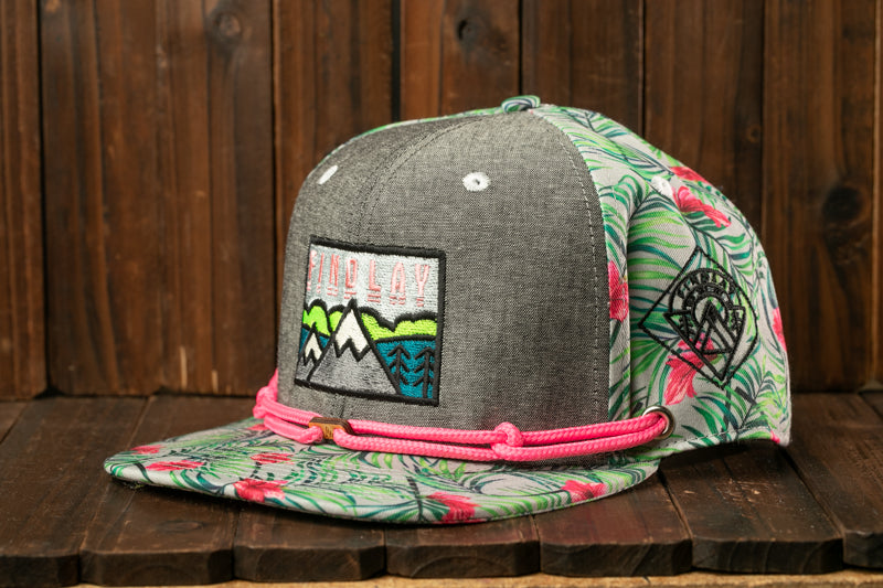 A gray baseball cap with a floral pattern and a mountain landscape embroidered on it, sitting on a wooden surface.