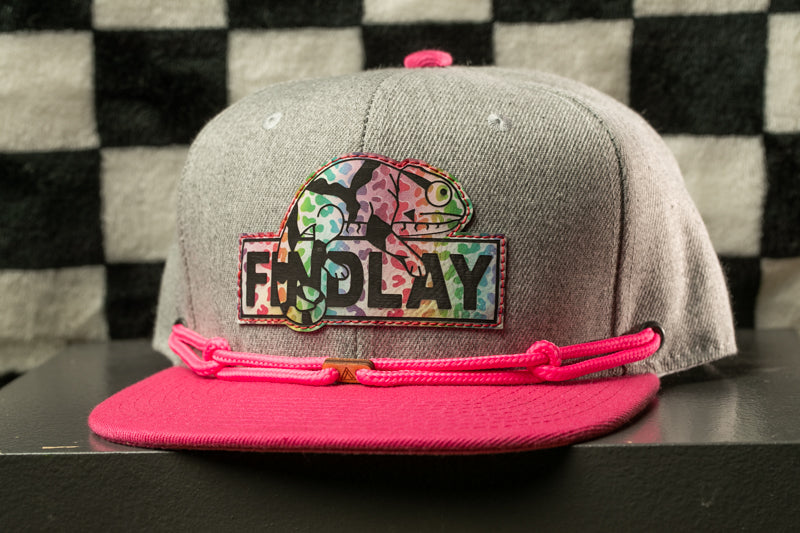 A gray baseball cap with a colorful graphic and the word "FINDLAY" printed on it, along with a pink string or strap.
