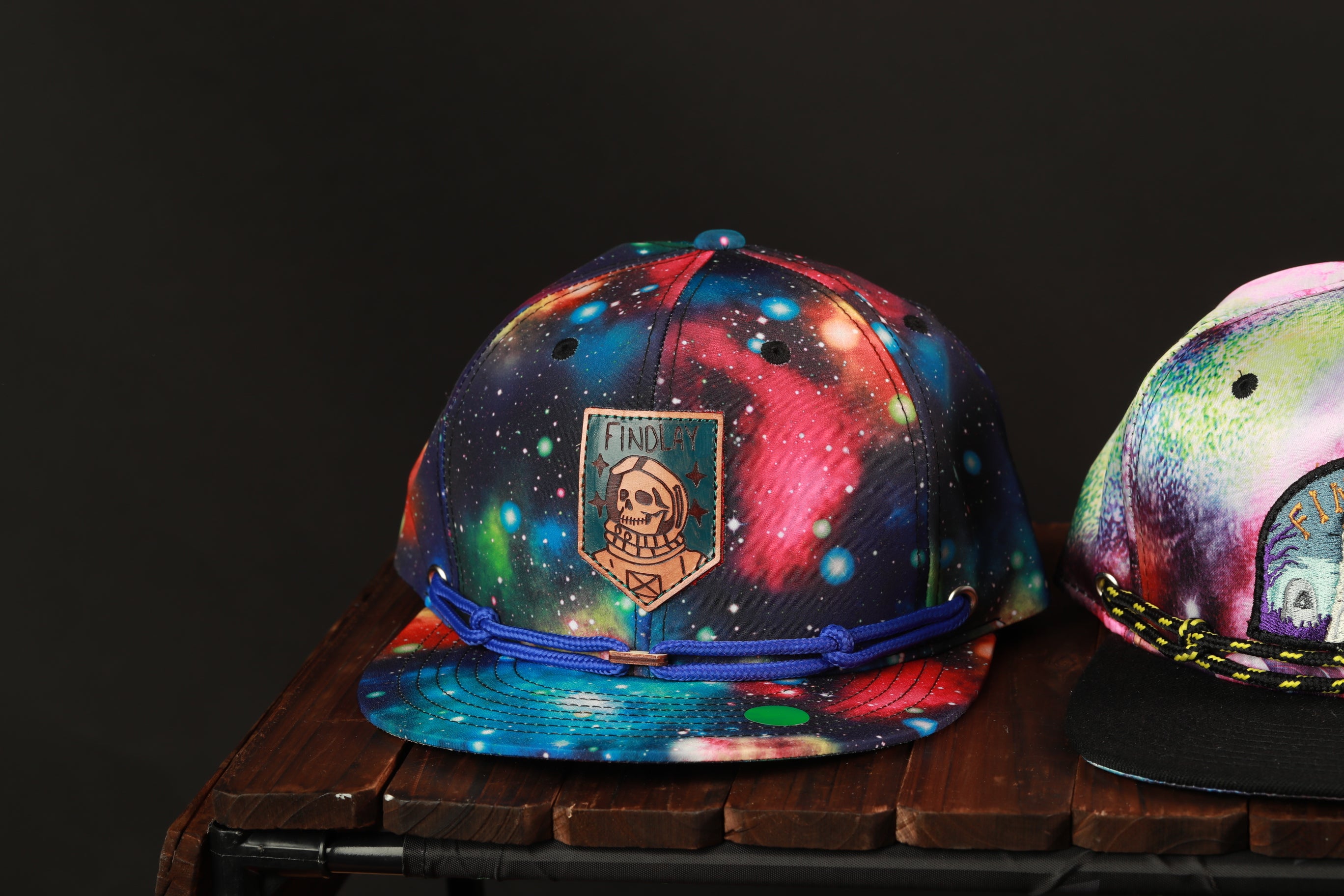 A colorful, space-themed baseball cap with a skull and star design sits on a wooden surface.