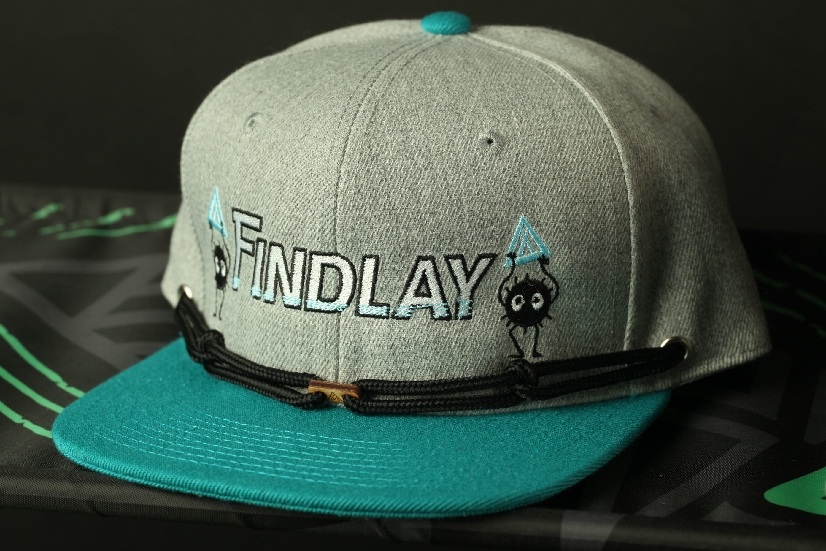 A grey baseball cap with teal brim and the word "FINDLAY" printed on it.