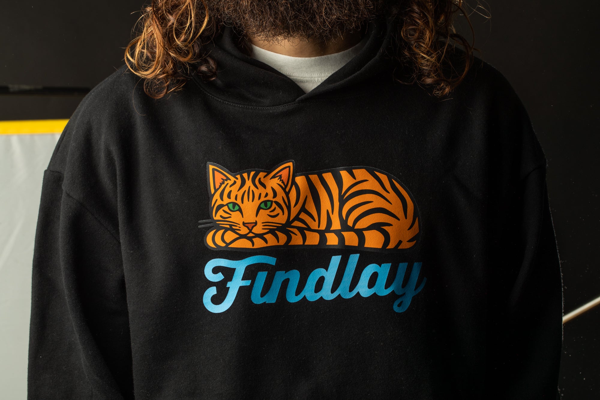 A person wearing a black hoodie with a graphic of a tiger cat and the word "Findlay" printed on it.