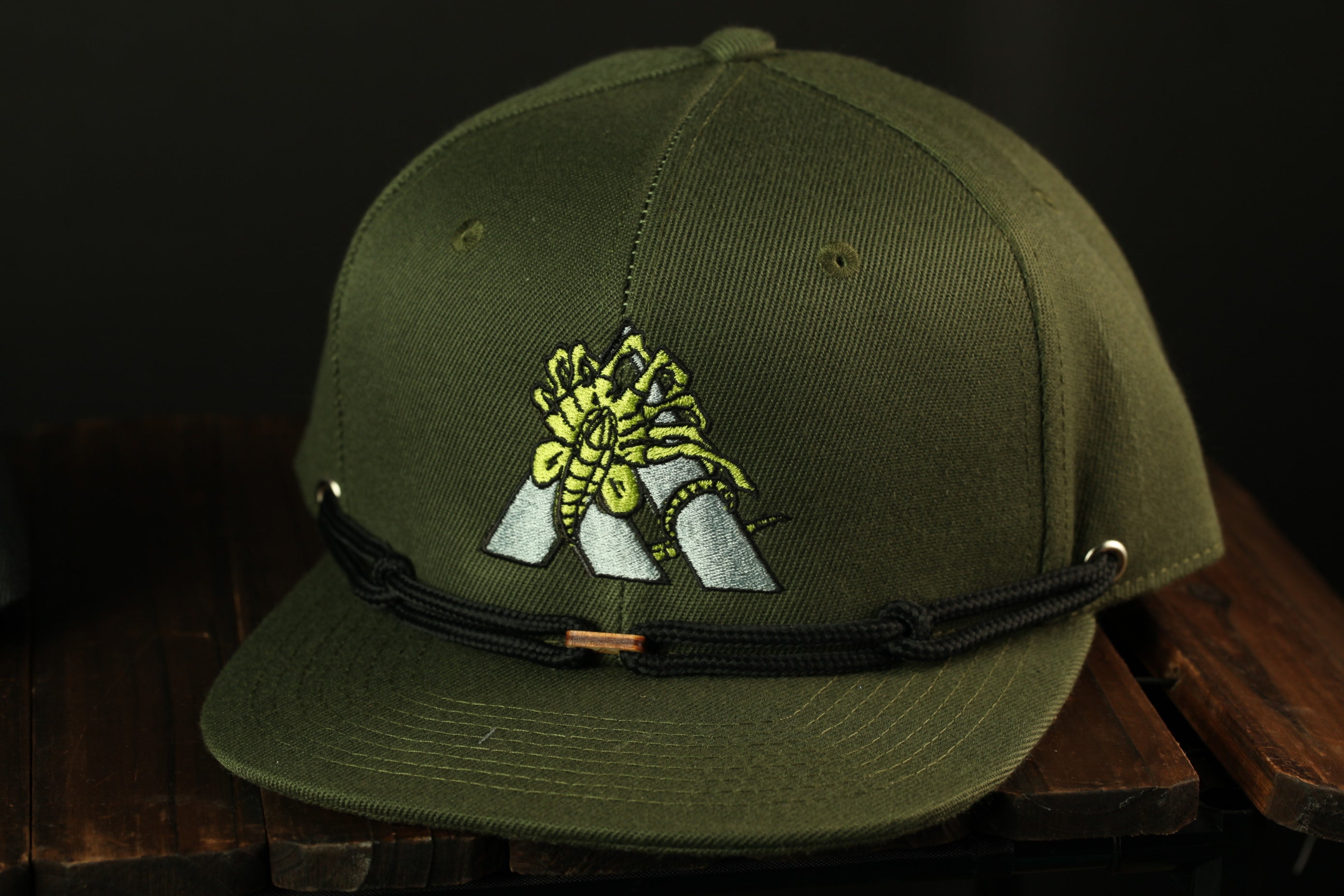 A green baseball cap with a black strap and a yellow and green insect design on the front.