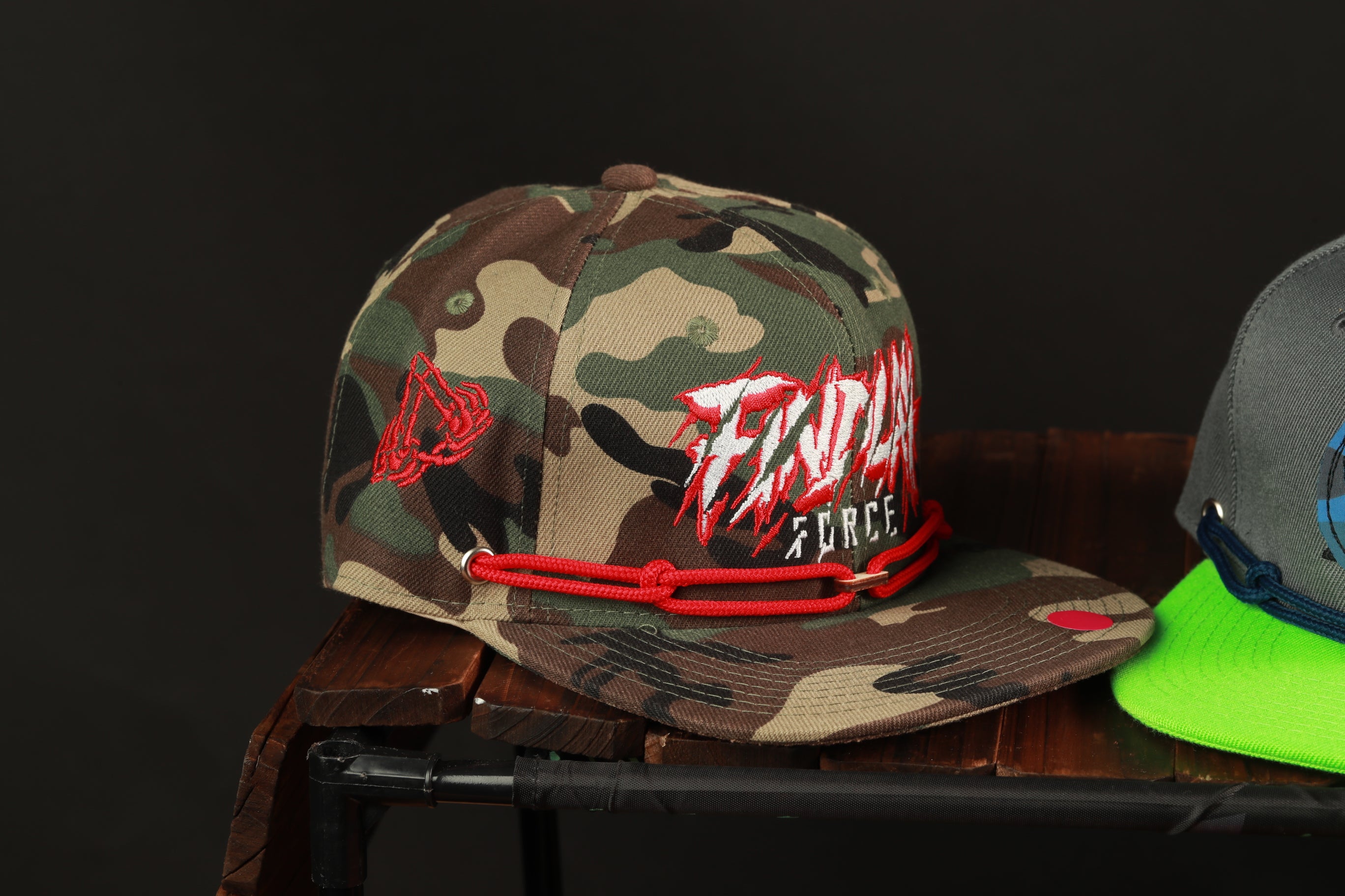 A camouflage baseball cap with the text "FINDING FORCE" printed on it, sitting on a wooden surface.