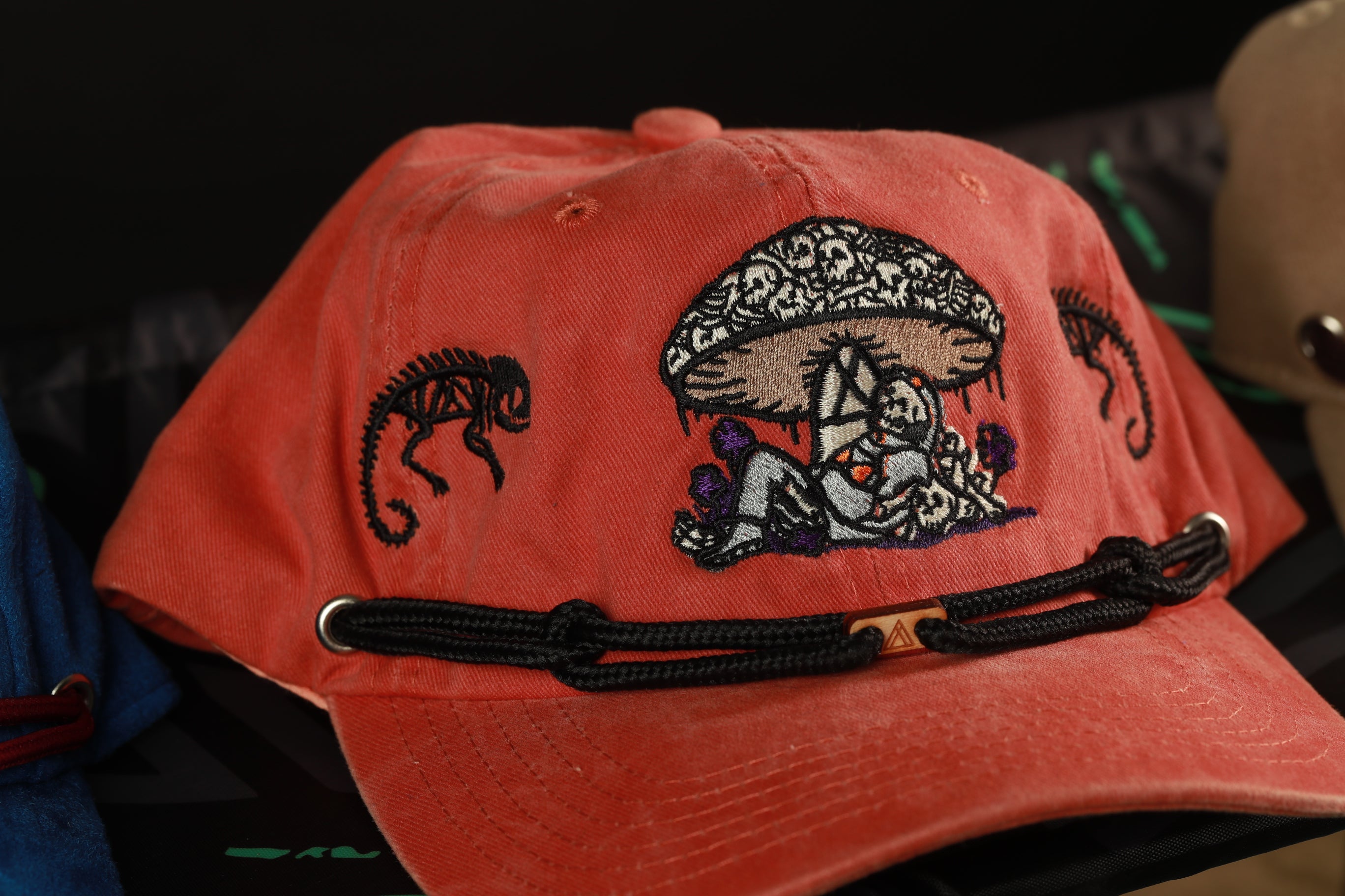 A red baseball cap with an embroidered design on the front, featuring a mushroom and a person sitting under it.