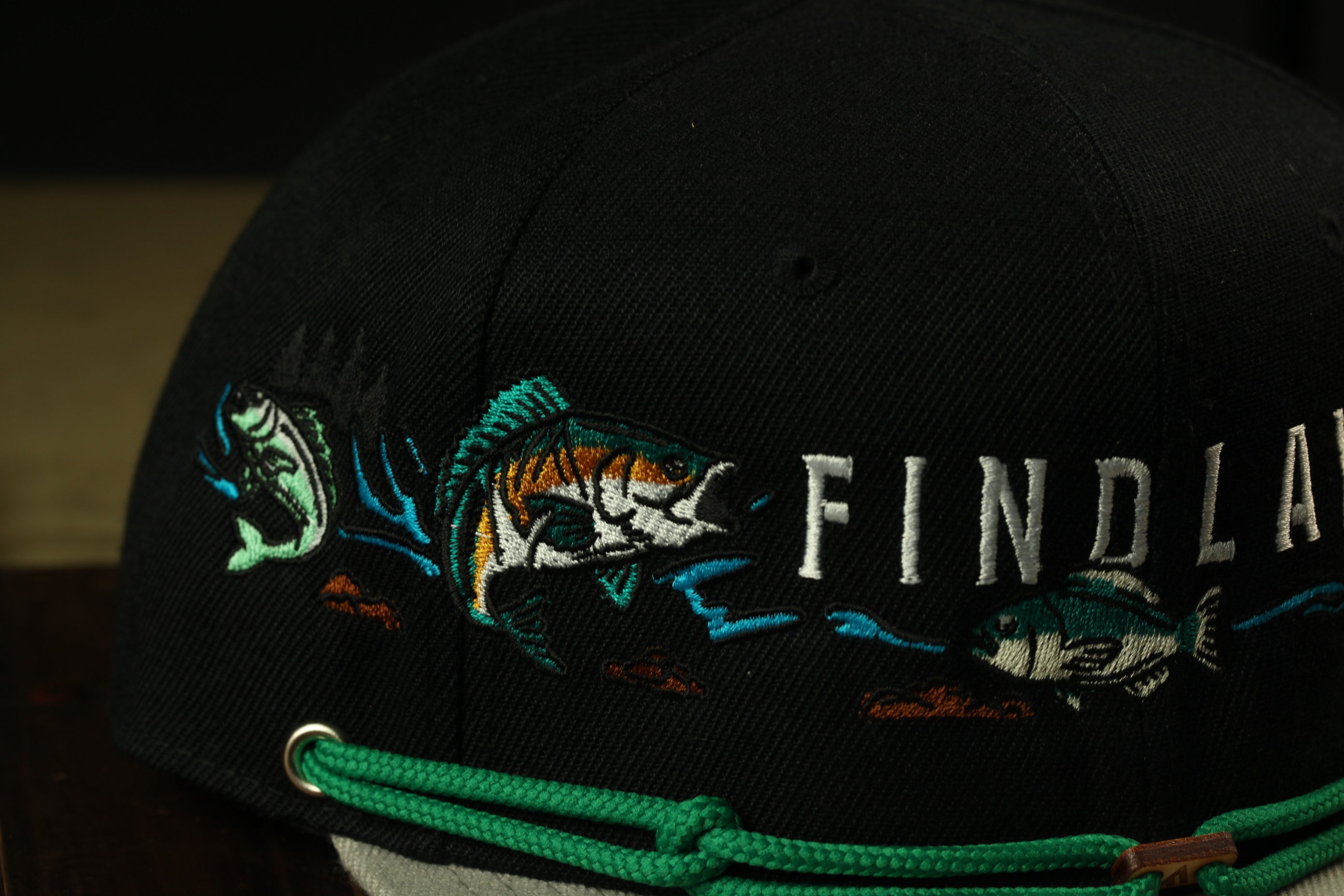 A close-up view of a black baseball cap with embroidered fish designs and the word "FINDLAND" printed on it.