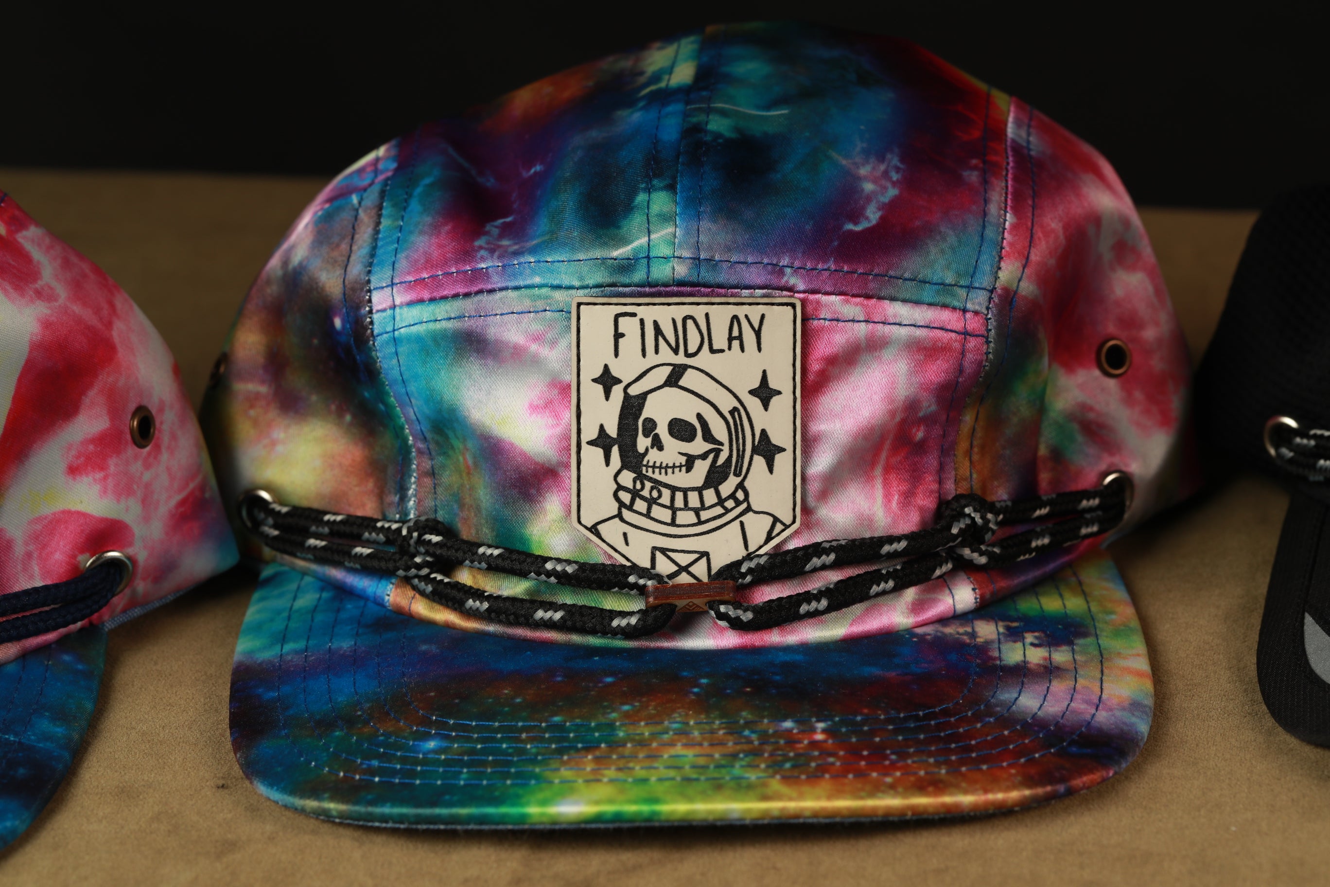 A colorful tie-dye baseball cap with a skull and star design, featuring the text "FINDLAY" on the front.
