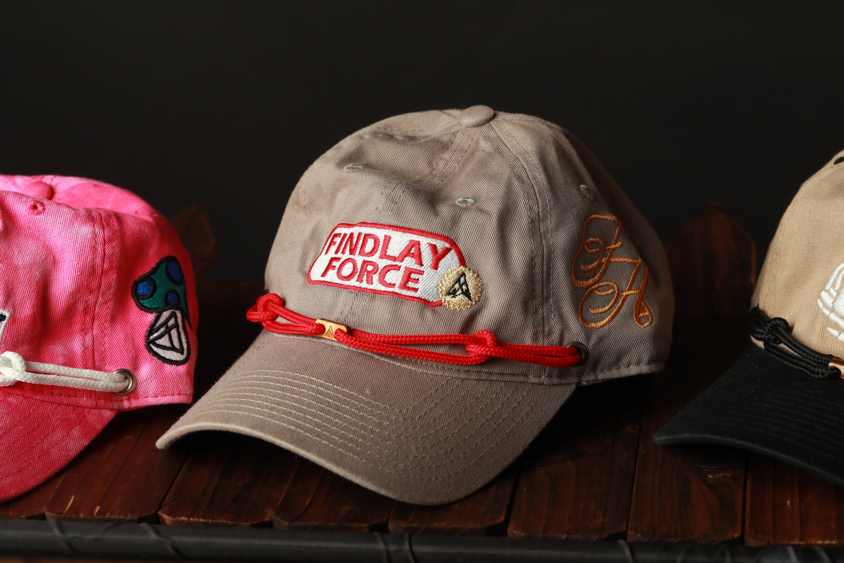 A collection of baseball caps with various designs and colors, including a gray cap with a red string and the text "FINDLAY FORCE" on it.