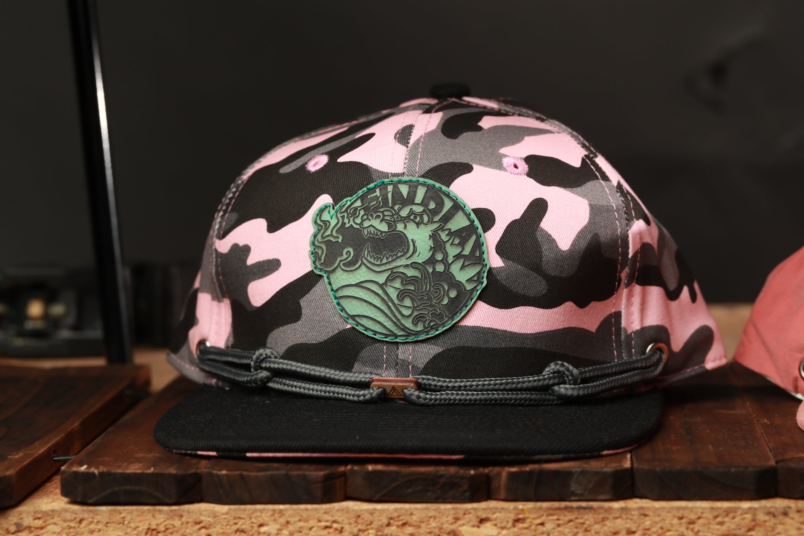 A pink and black camouflage baseball cap with a green circular patch on the front.