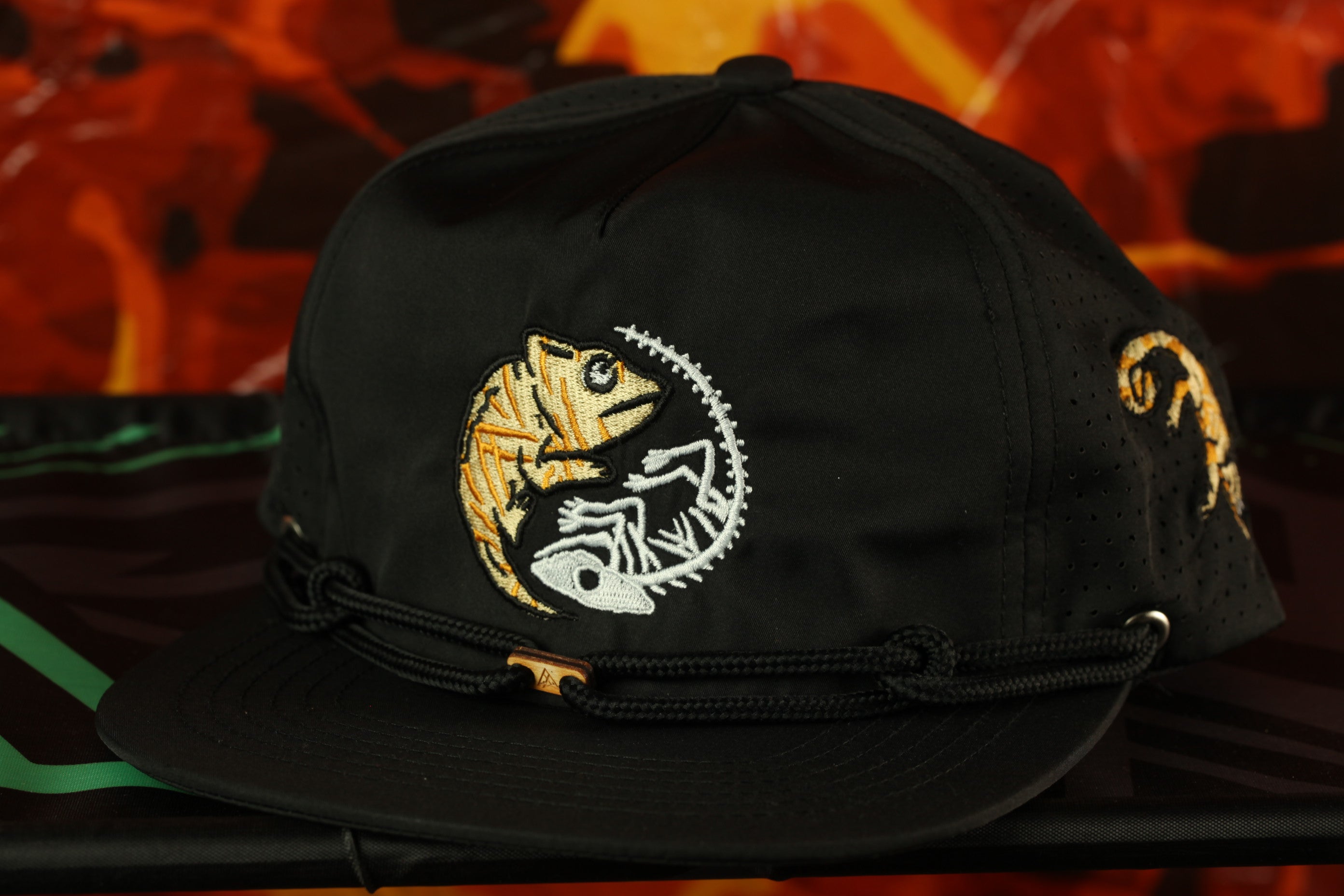 A black baseball cap with a white and yellow chameleon design on the front.