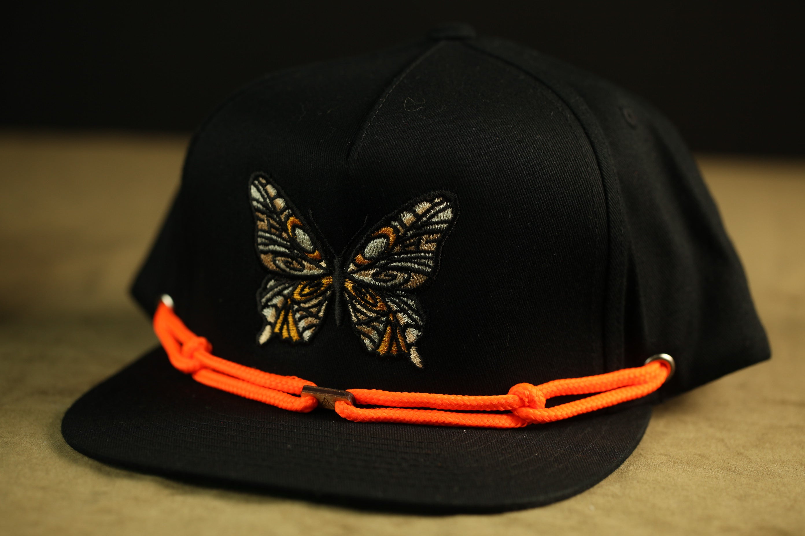 A black baseball cap with an orange braided chain around the brim.