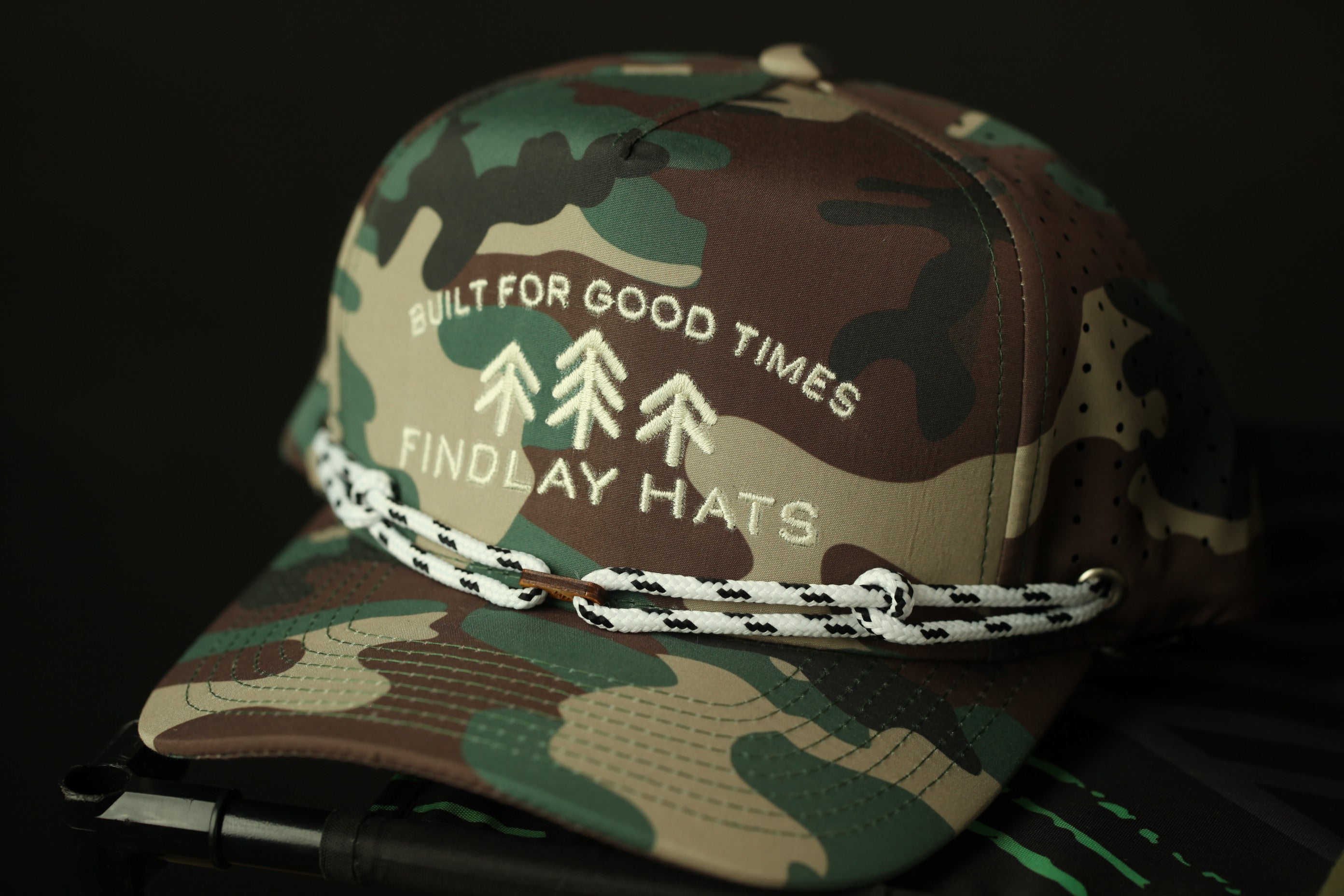 A camouflage baseball cap with the text "BUILT FOR GOOD TIMES FINDLAY HATS" printed on it.