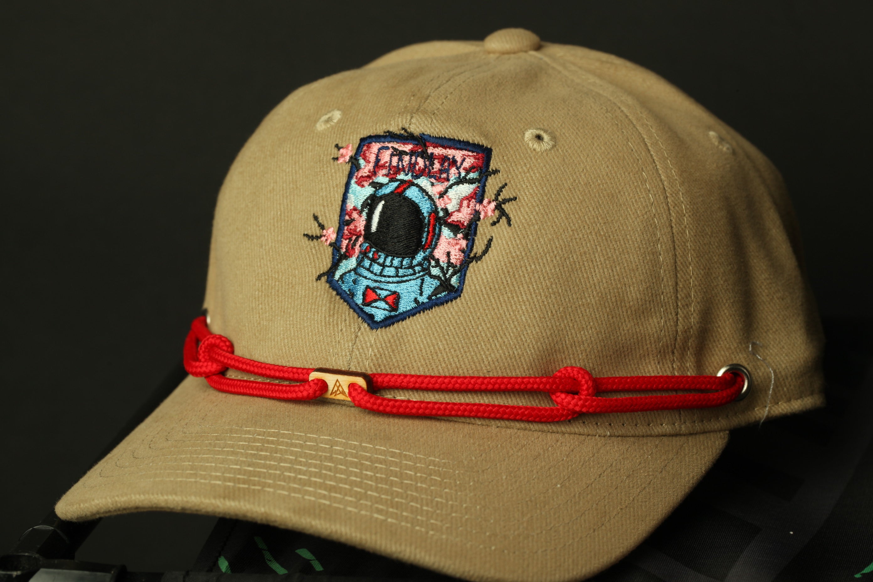 A beige baseball cap with a red string and a patch featuring a blue and white design on the front.