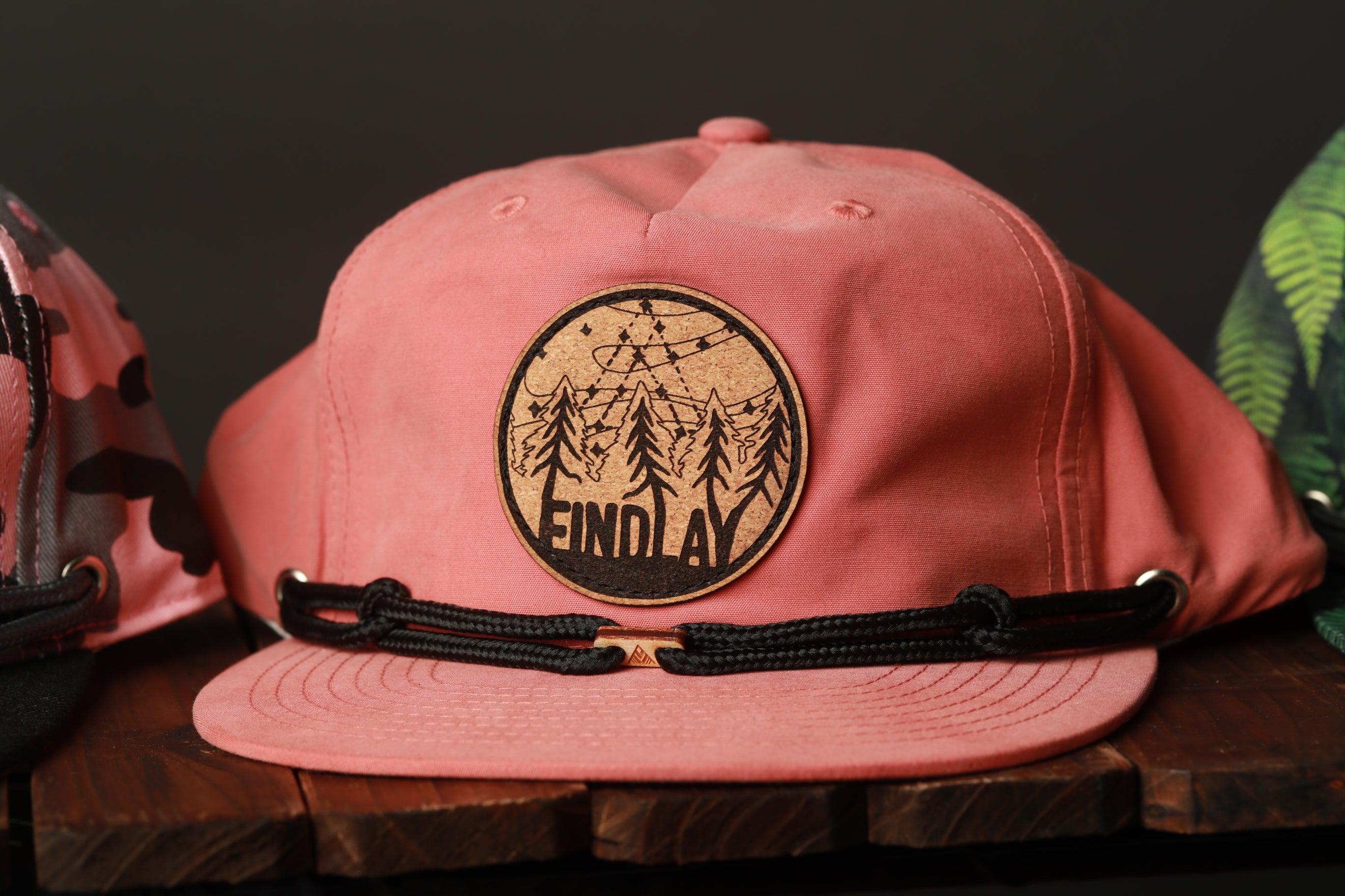 A pink baseball cap with a circular patch on the front displaying the word "FINDlay".