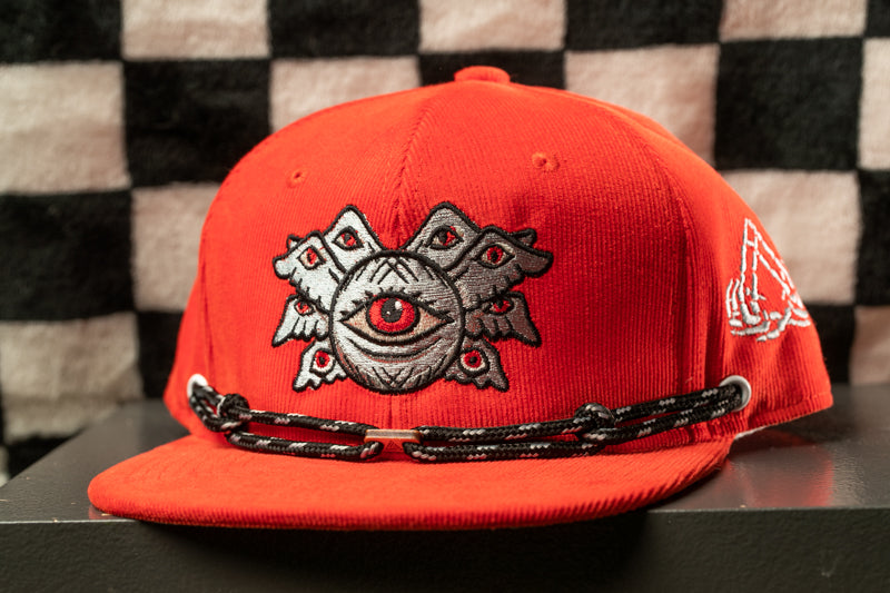 A red baseball cap with a black and white checkered pattern and an eye design on the front.