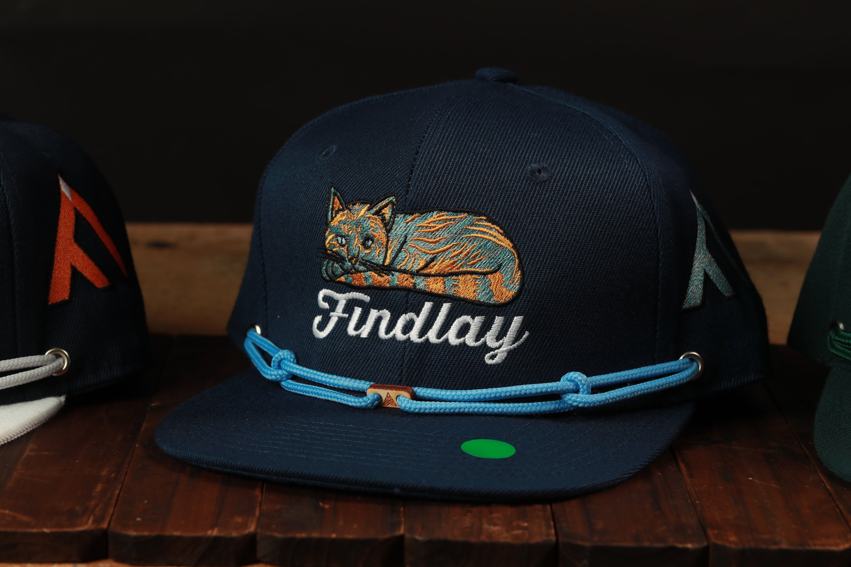 A navy blue baseball cap with a cat embroidered on it, sitting on a wooden surface.