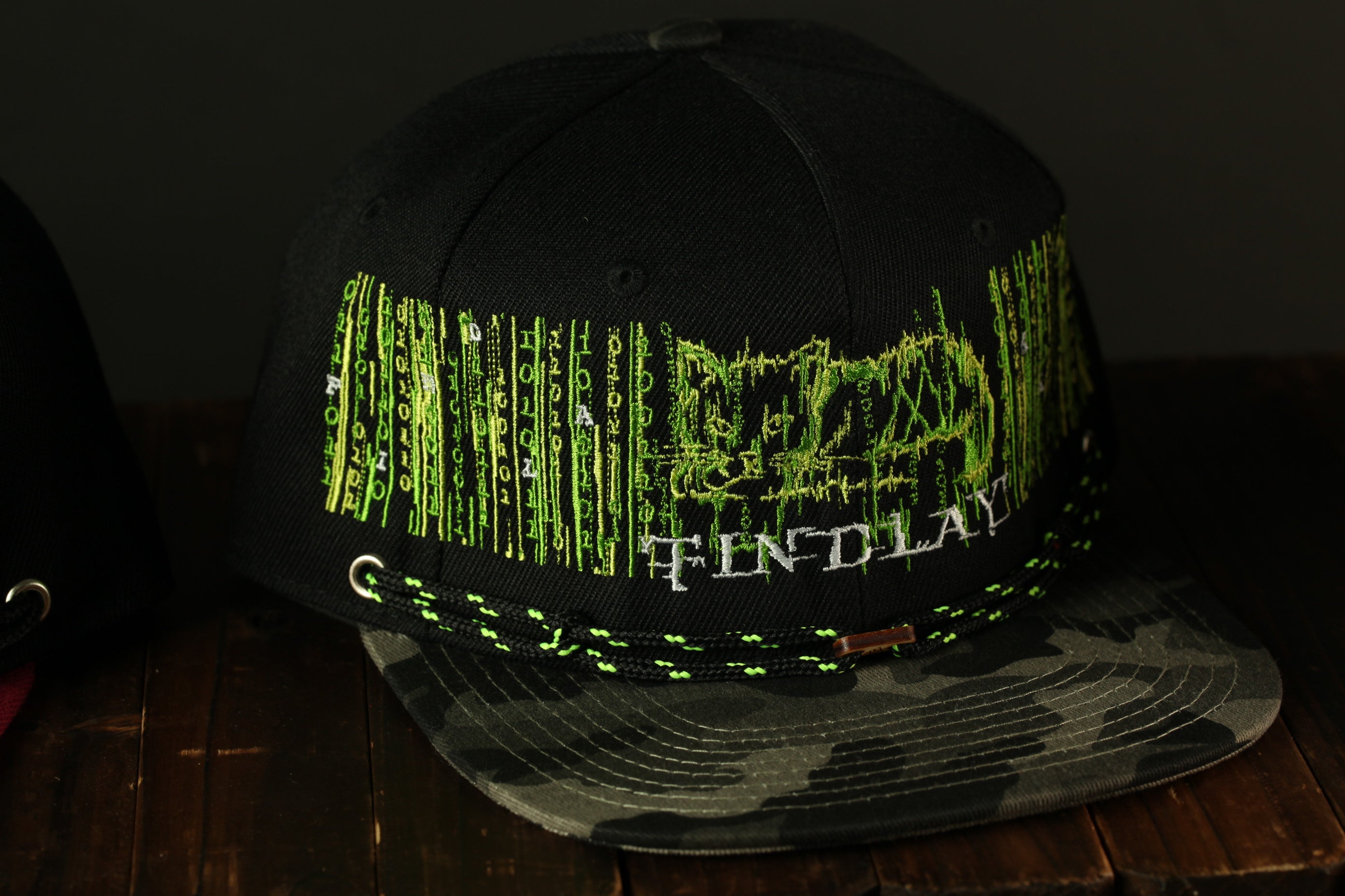 A black baseball cap with green text and graphics on it, placed on a wooden surface.