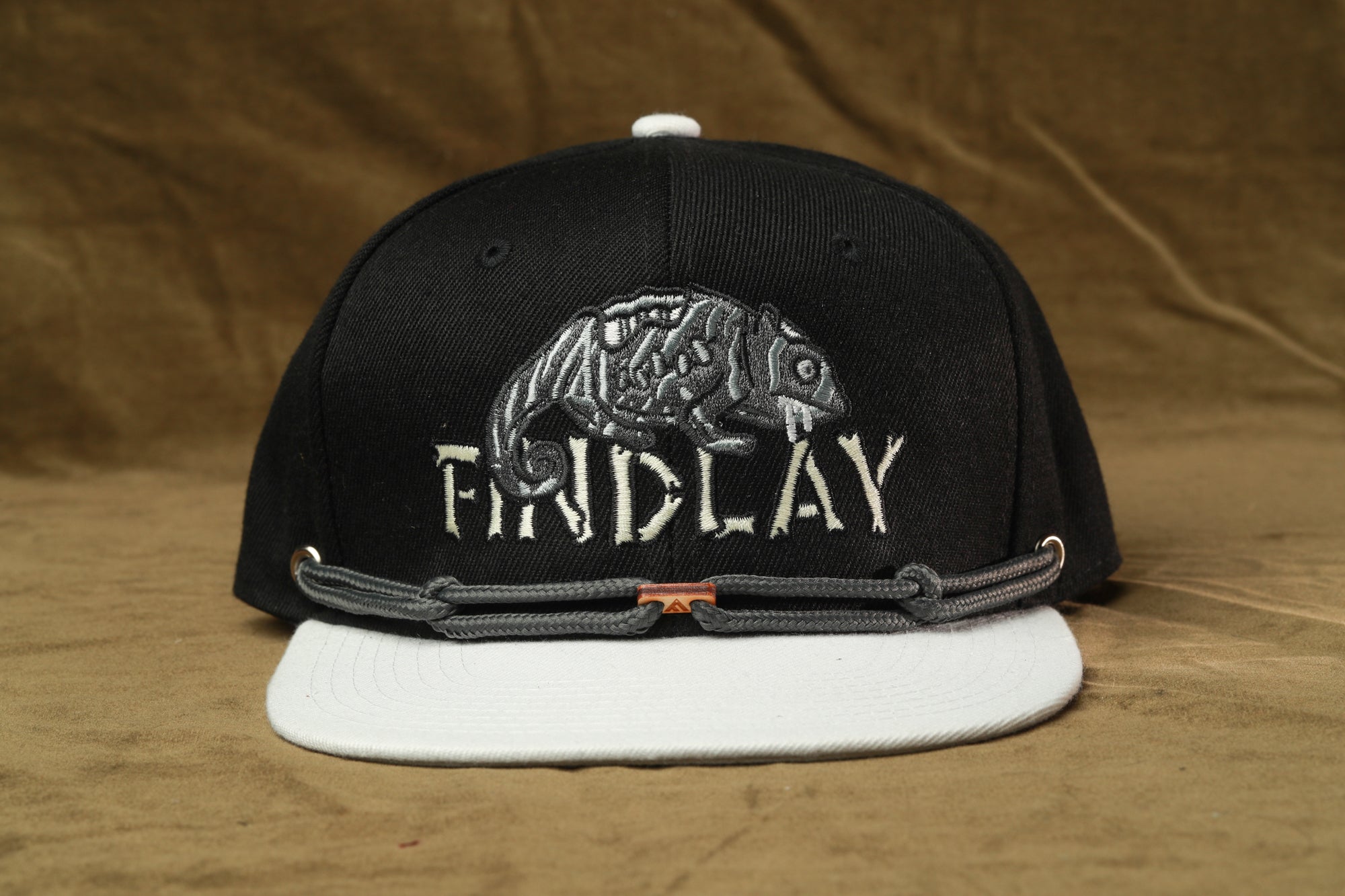 A black baseball cap with a white brim and a white logo on the front, featuring a stylized chameleon design.