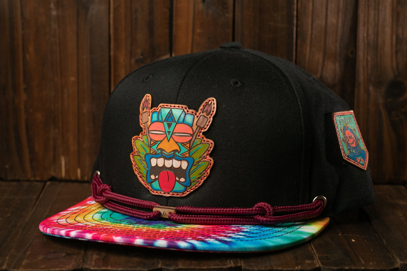 A black baseball cap with a colorful, abstract design on the front, including a face and various geometric shapes.