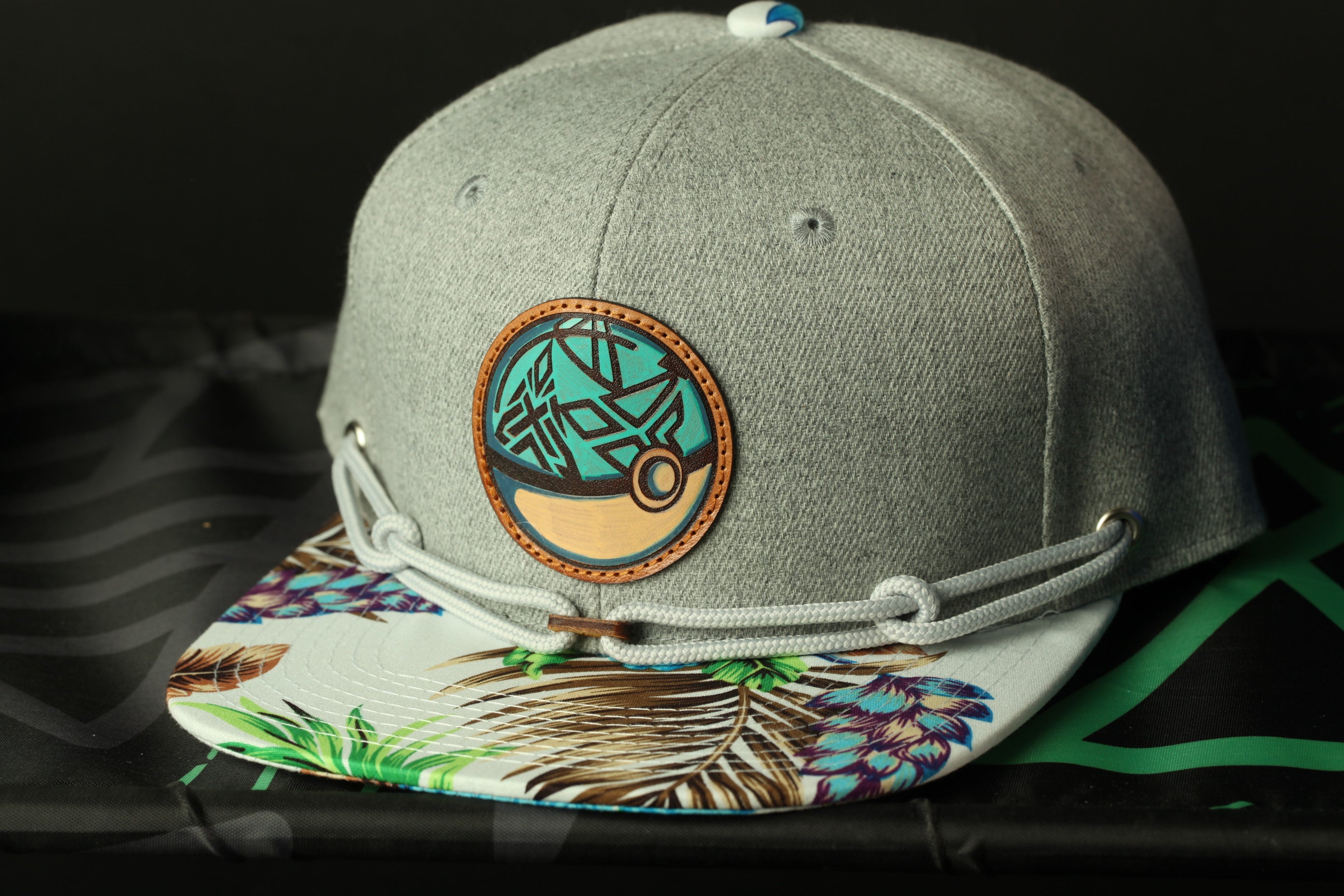 A gray baseball cap with a tropical leaf pattern and a circular patch on the front.