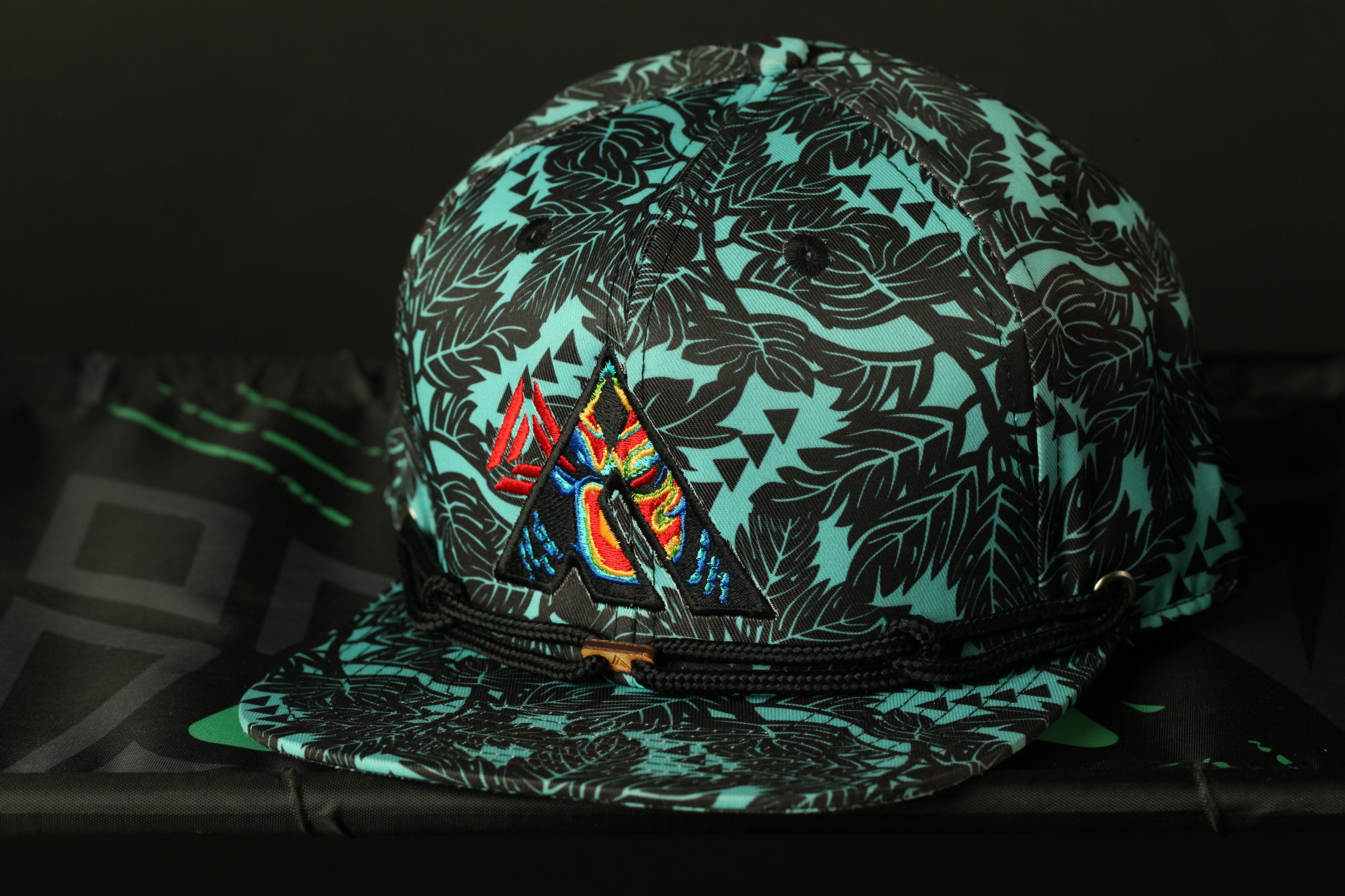 A colorful, patterned baseball cap with a tropical leaf design is displayed against a dark background.