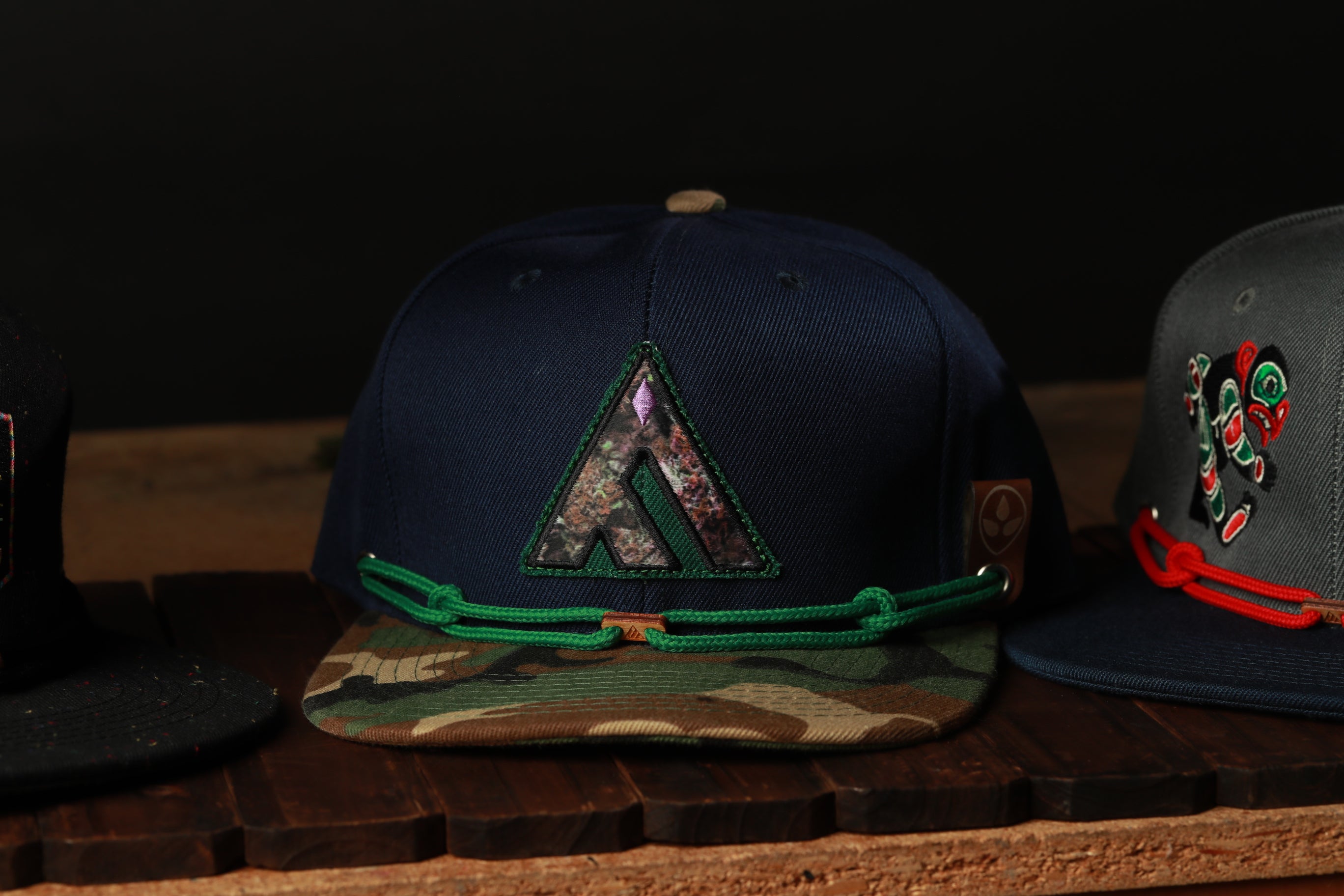 A collection of baseball caps with various designs and colors, including a dark blue cap with a camouflage pattern and a red and black cap with a floral design.