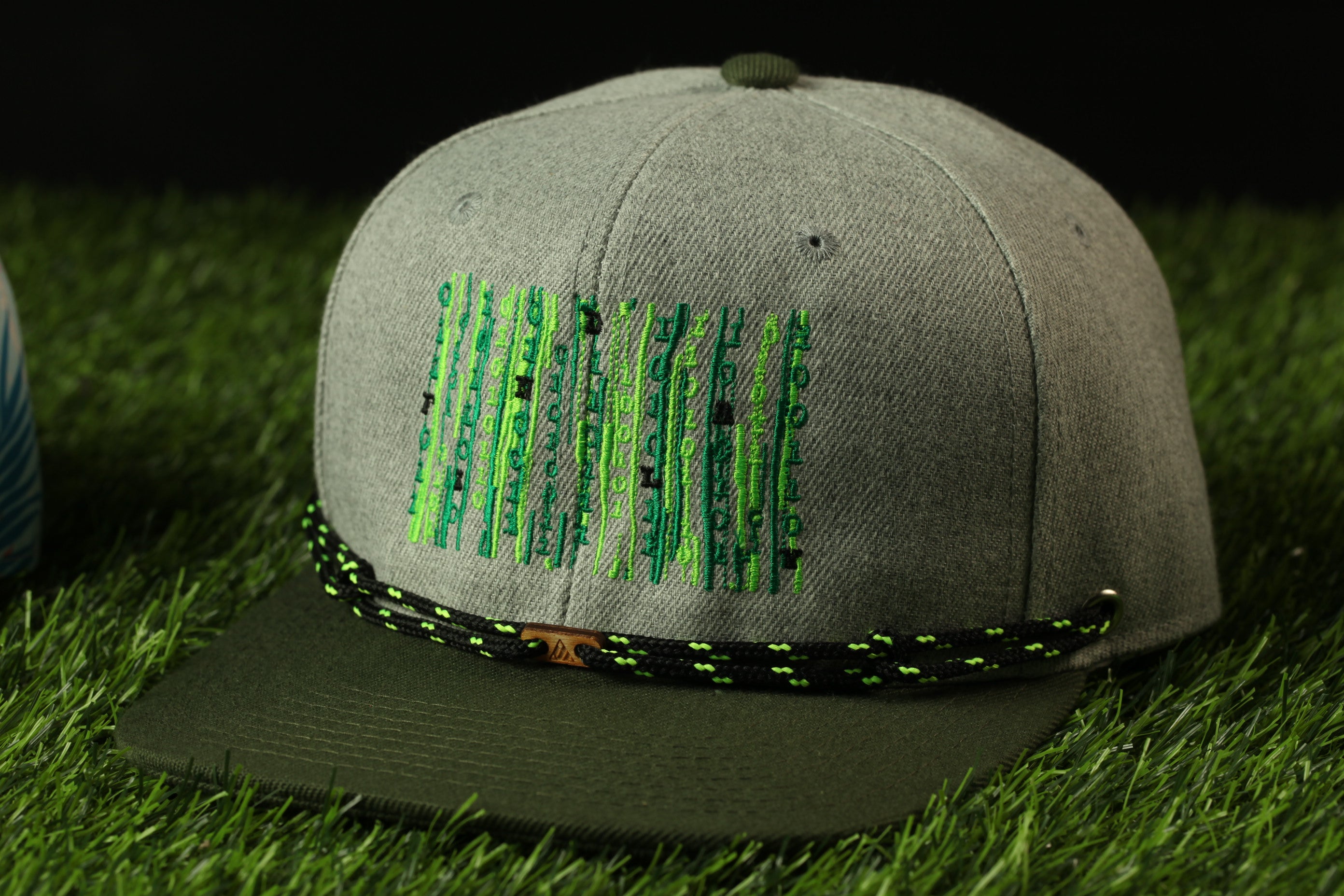 A gray baseball cap with a green and black braided strap, placed on a grassy surface.