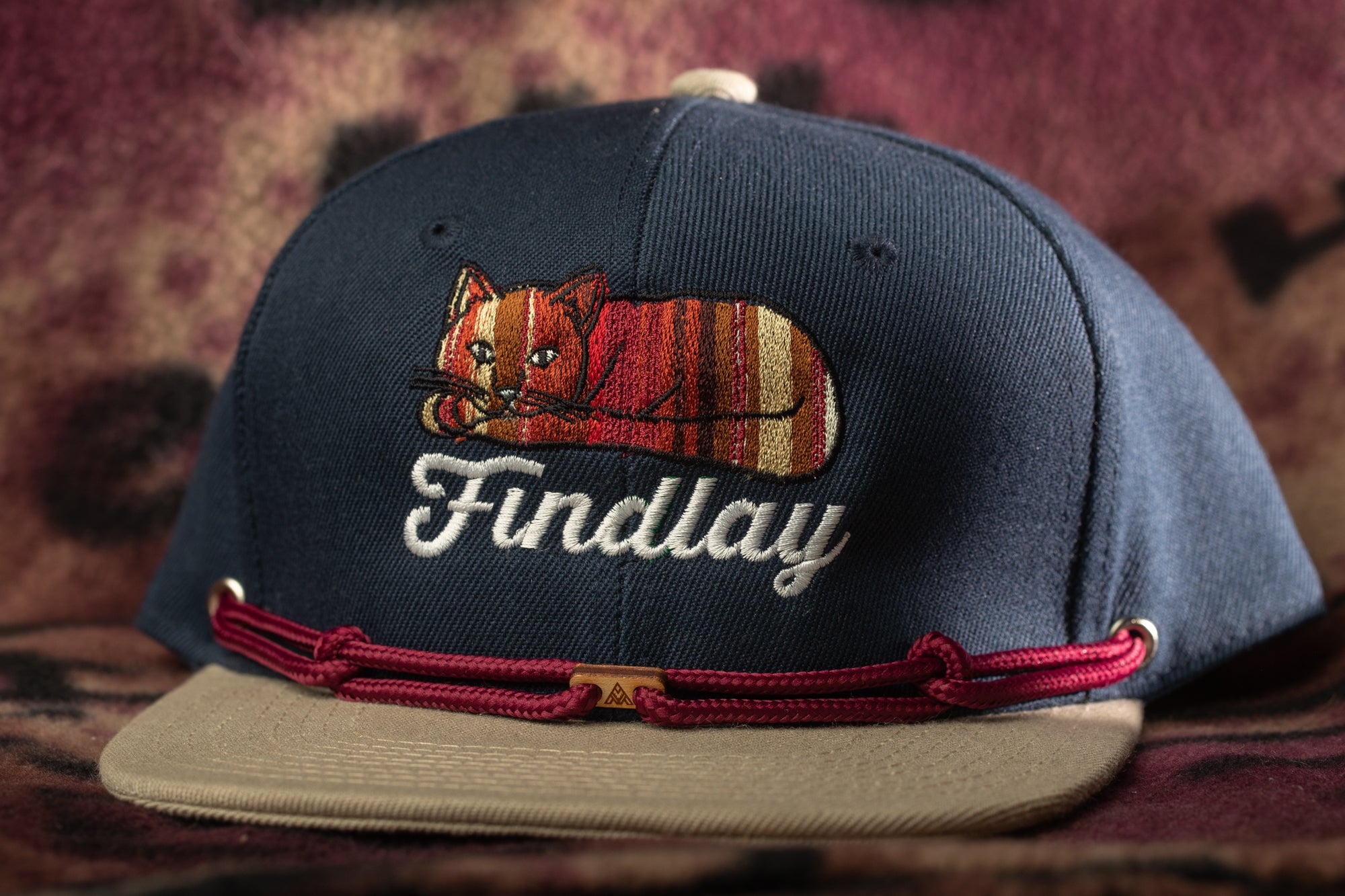 A navy blue baseball cap with a cat embroidered on it, and the word "Findlay" written on it.