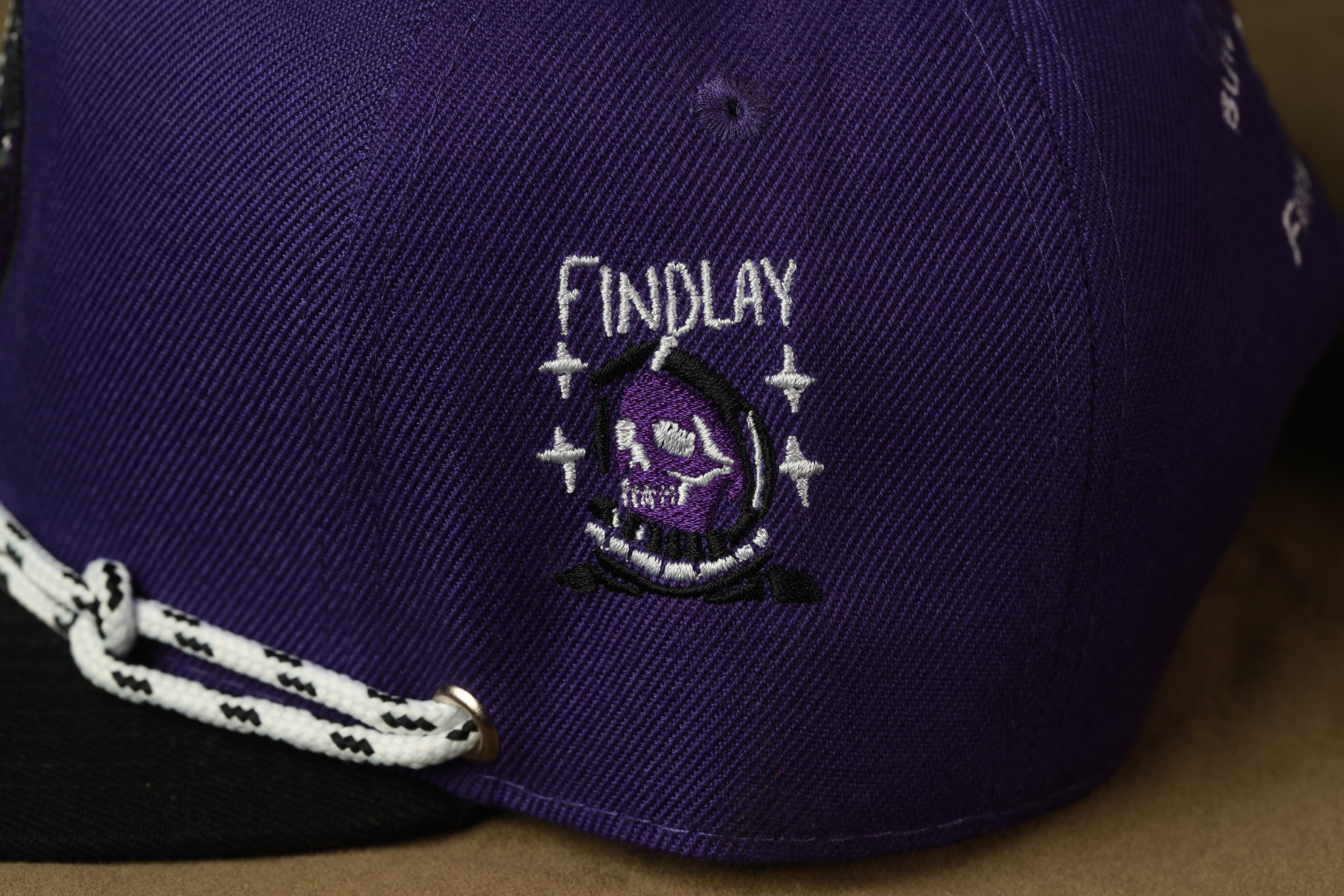 A close-up view of a purple baseball cap with a white logo on the front.