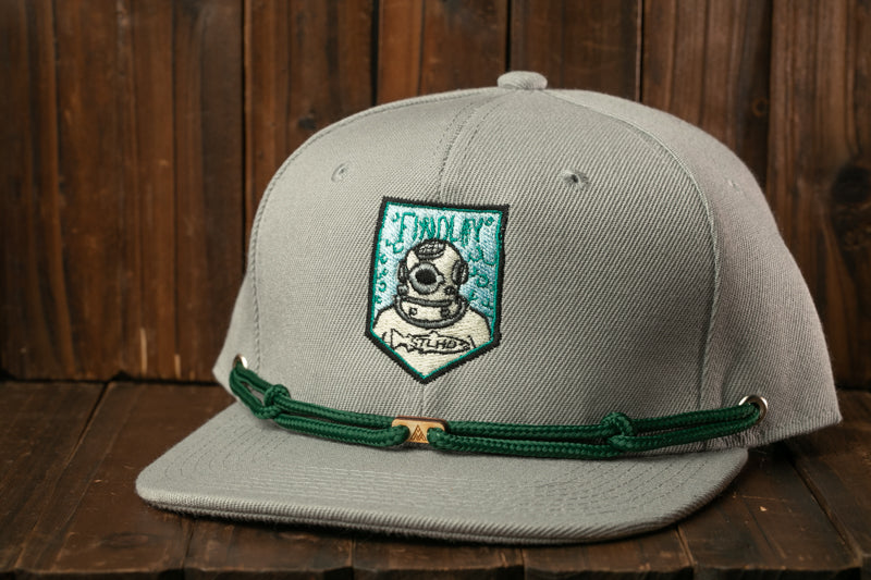 A gray baseball cap with a green adjustable strap and a patch featuring a diving suit and the word "DIVE" on a wooden background.