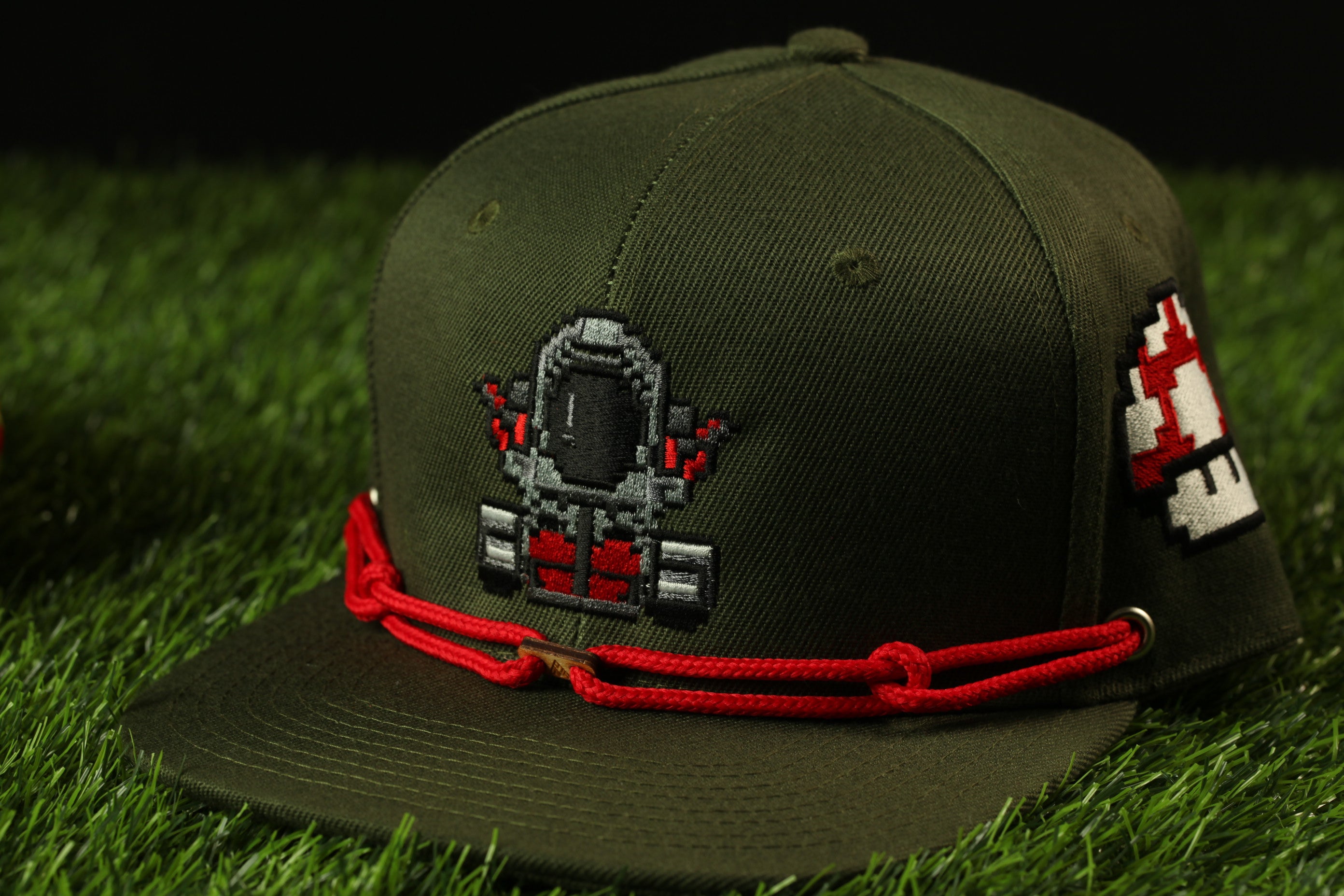 A green baseball cap with a red string and a pixelated character design on the front.