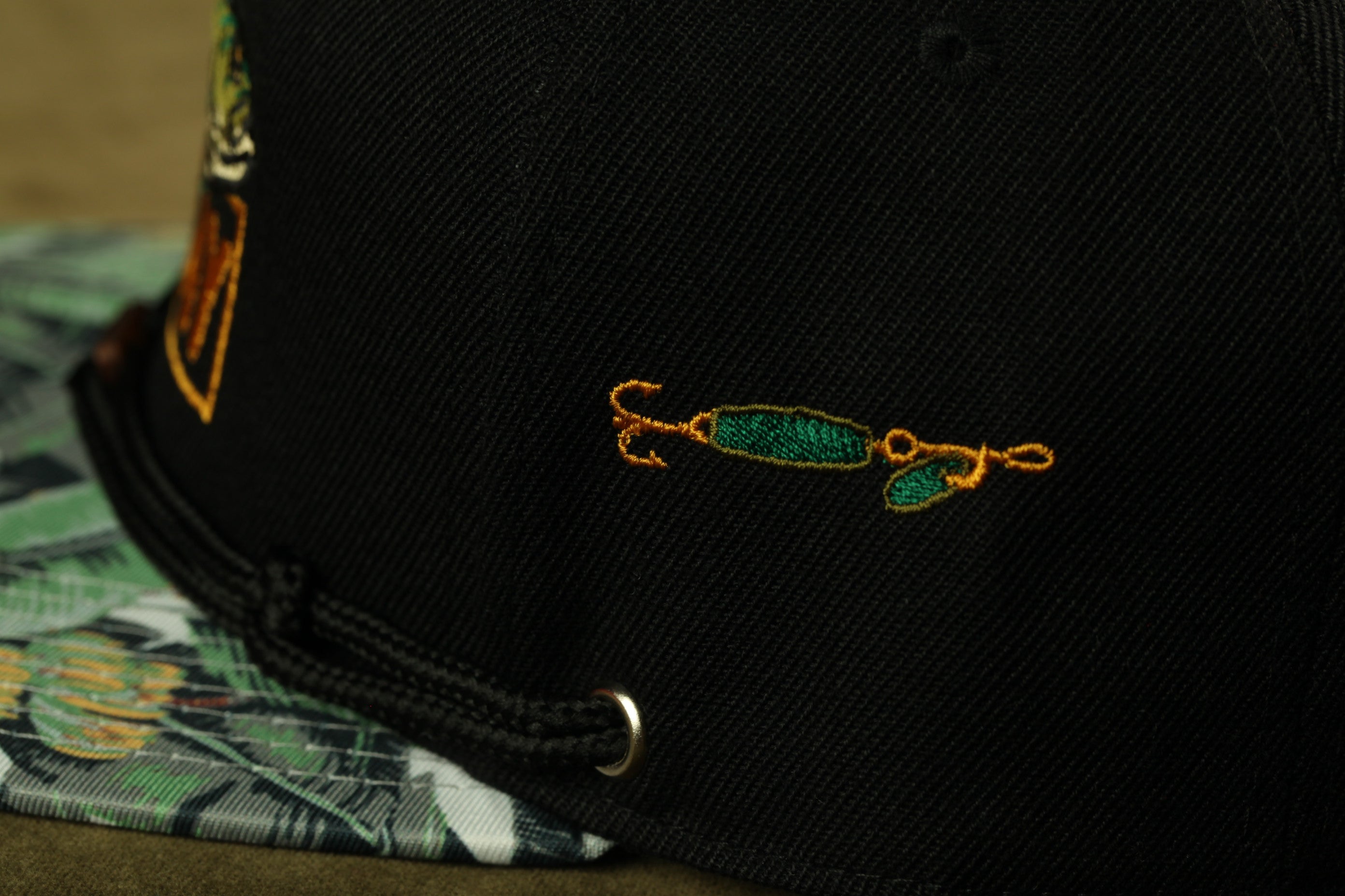 a close-up view of a black baseball cap with a green and yellow embroidered design on the front.