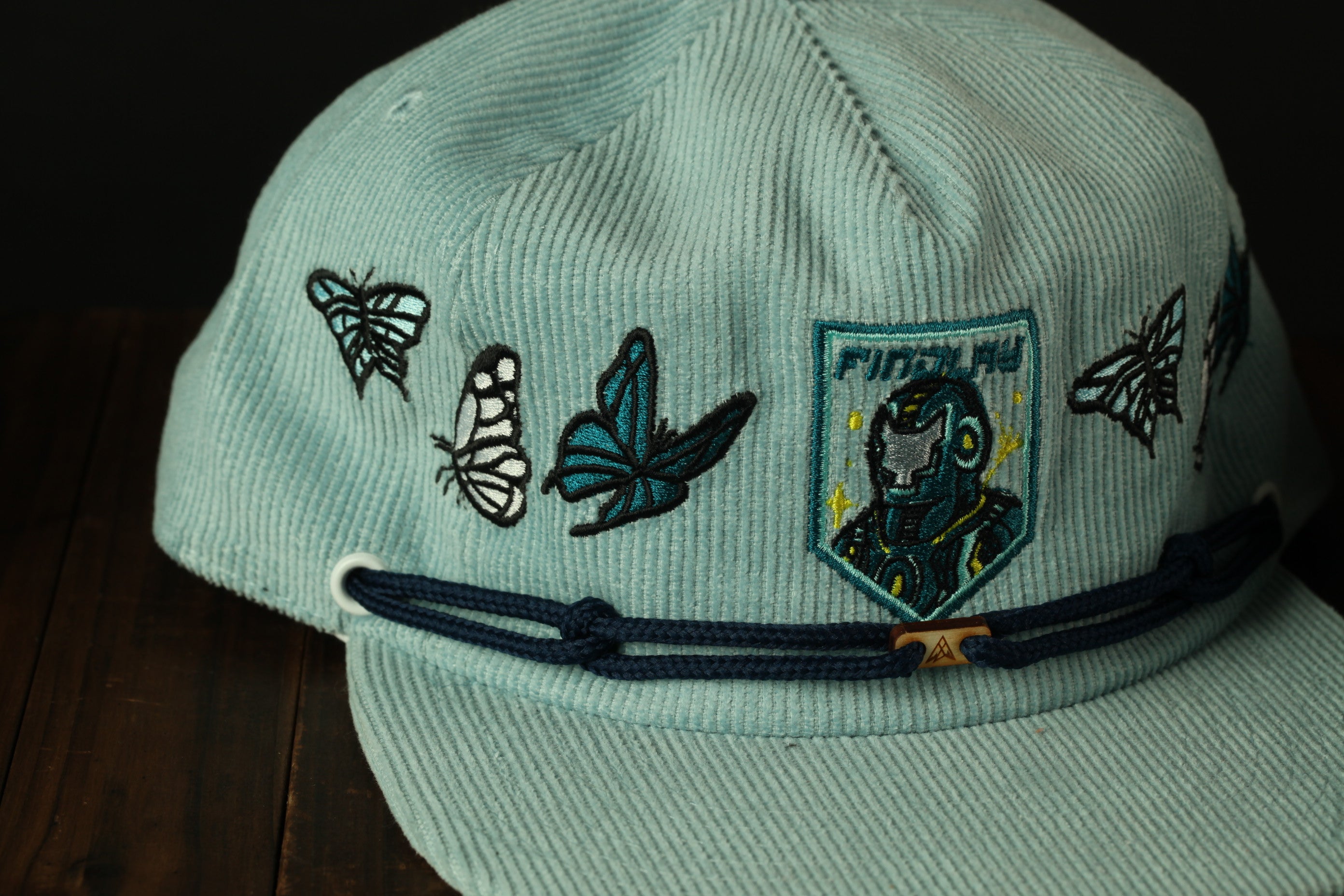 A light blue baseball cap with various embroidered designs, including butterflies and a character, is shown in the image.