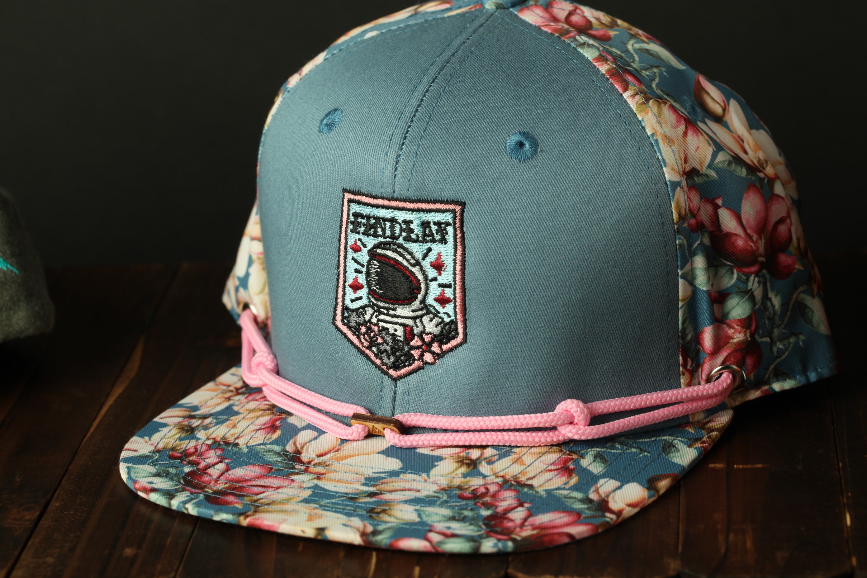 A floral-patterned baseball cap with a patch featuring a graphic design and the text "FIND A FALL".