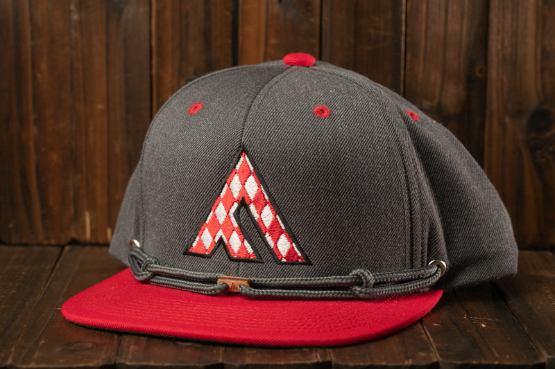A gray baseball cap with a red and white checkered logo on the front, placed on a wooden surface.