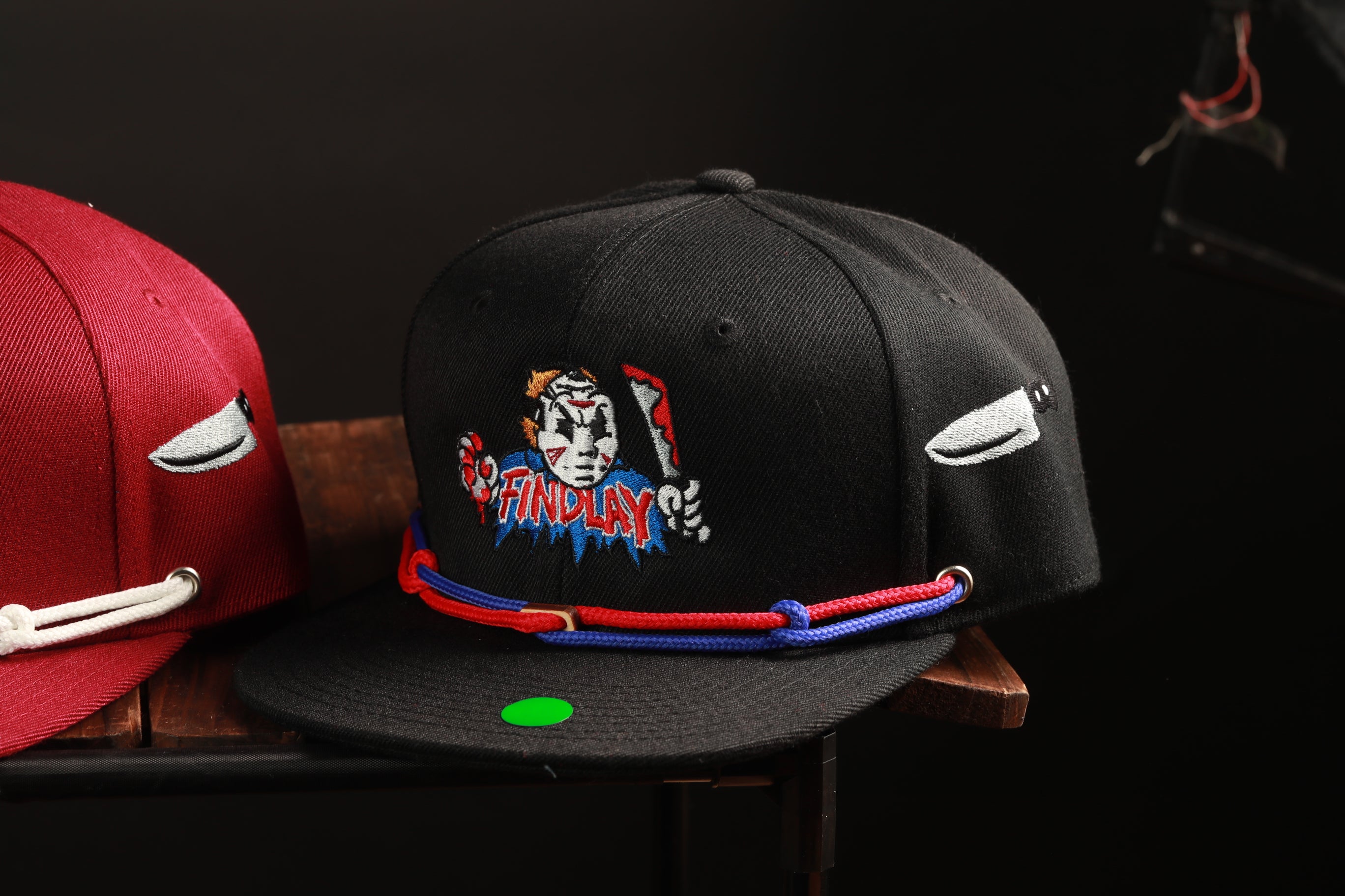 two baseball caps, one black and one red, placed on a wooden surface.