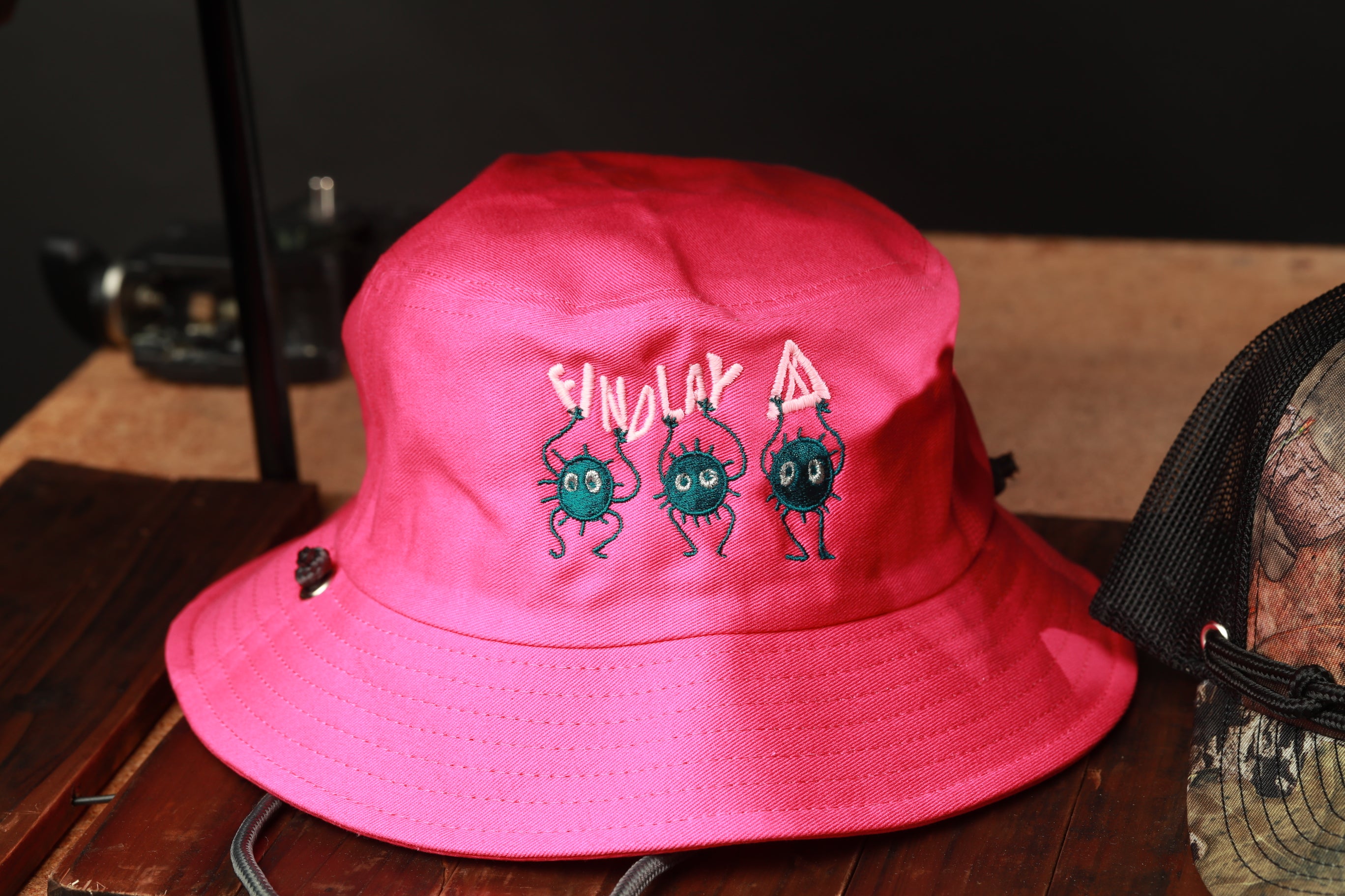 A bright pink bucket hat with a cartoon-style design featuring three small green insects.