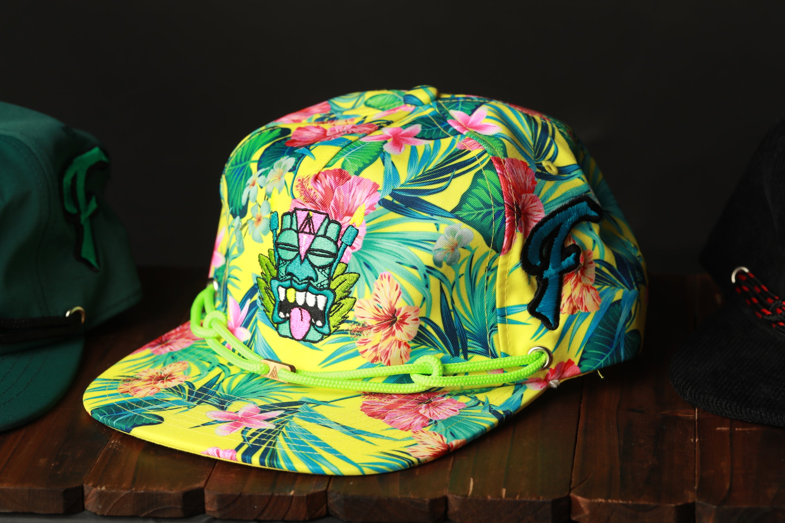 A colorful, floral-patterned baseball cap with a graphic design on the front, displayed on a wooden surface.