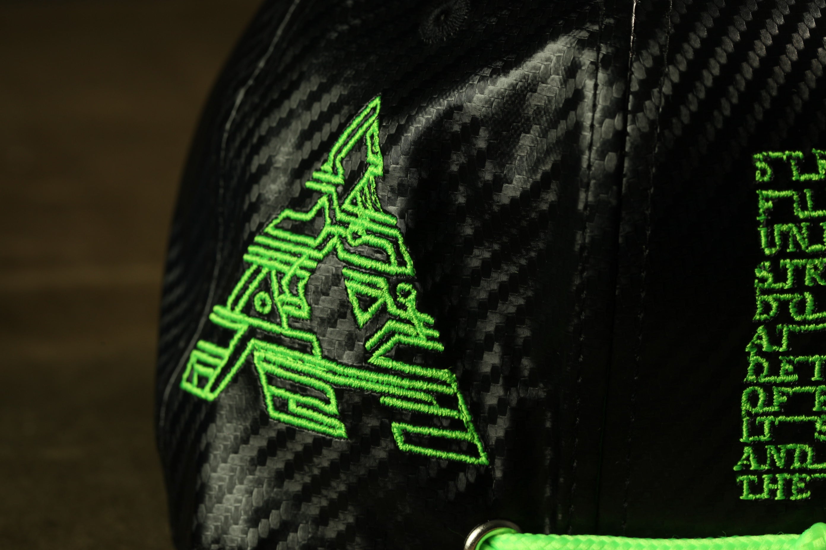 a close-up view of a black baseball cap with a green embroidered logo on it.