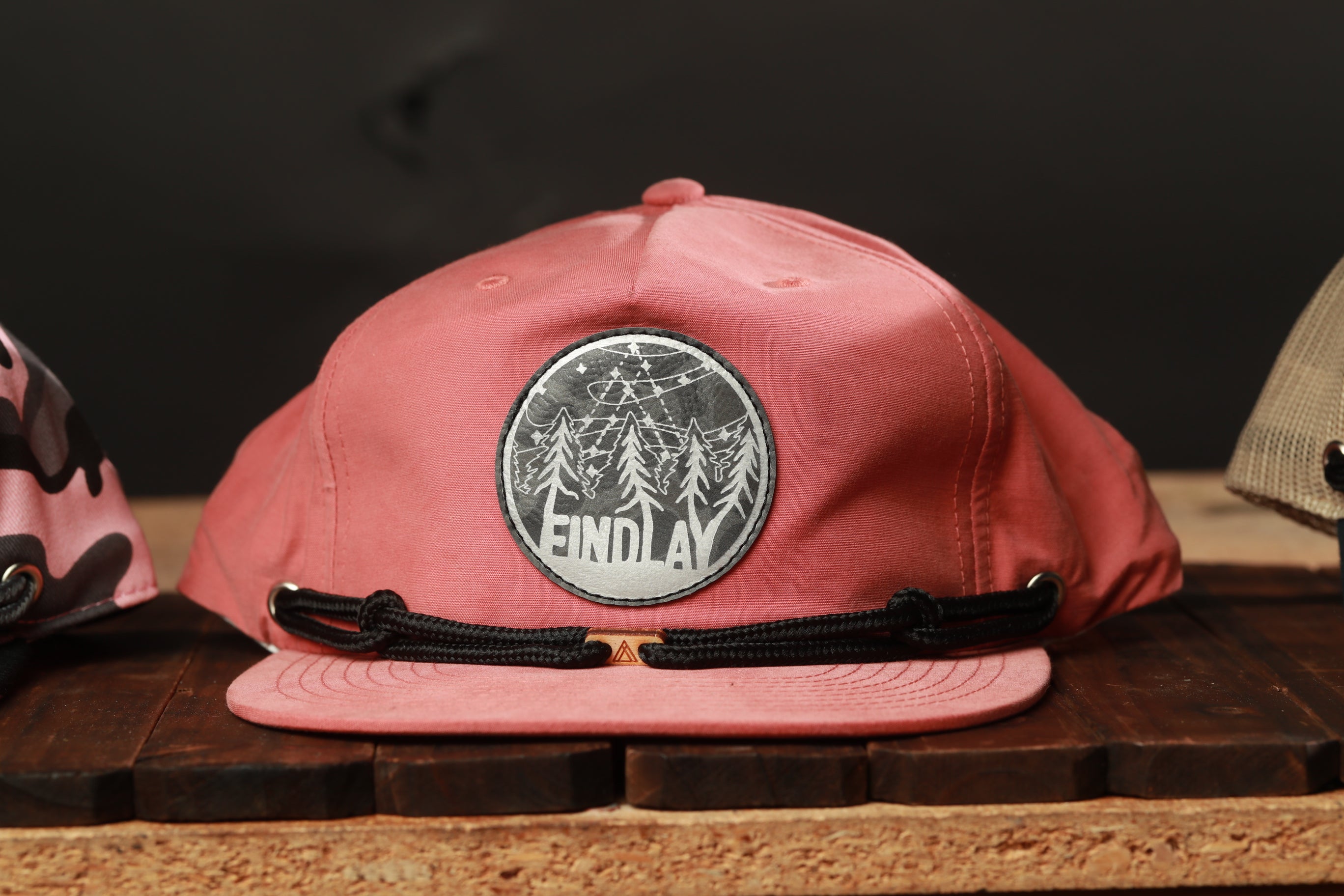 A pink baseball cap with a circular patch on the front displaying the word "FINDLAY".