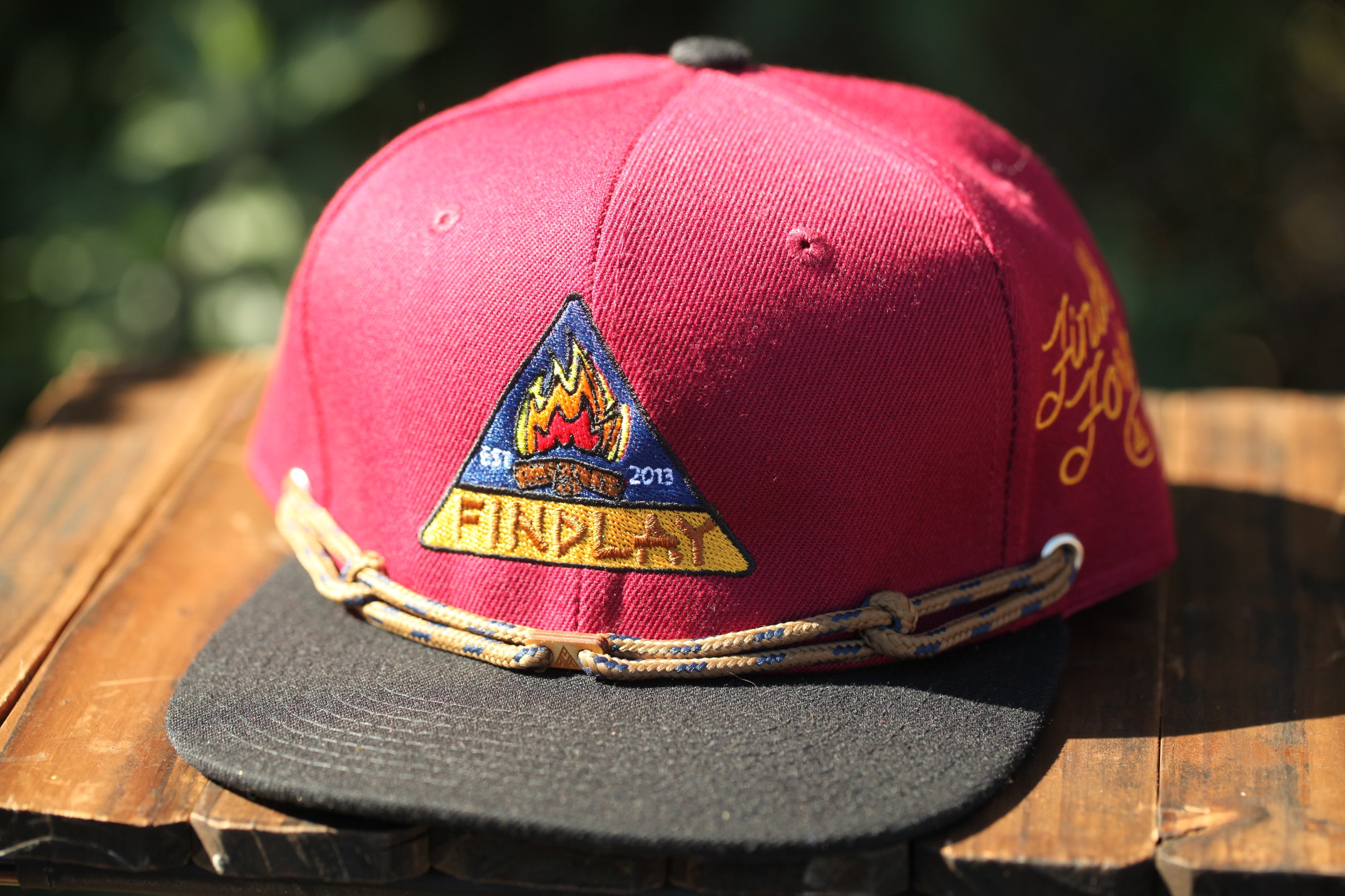A red baseball cap with a black brim and a yellow and blue logo on the front, sitting on a wooden surface.