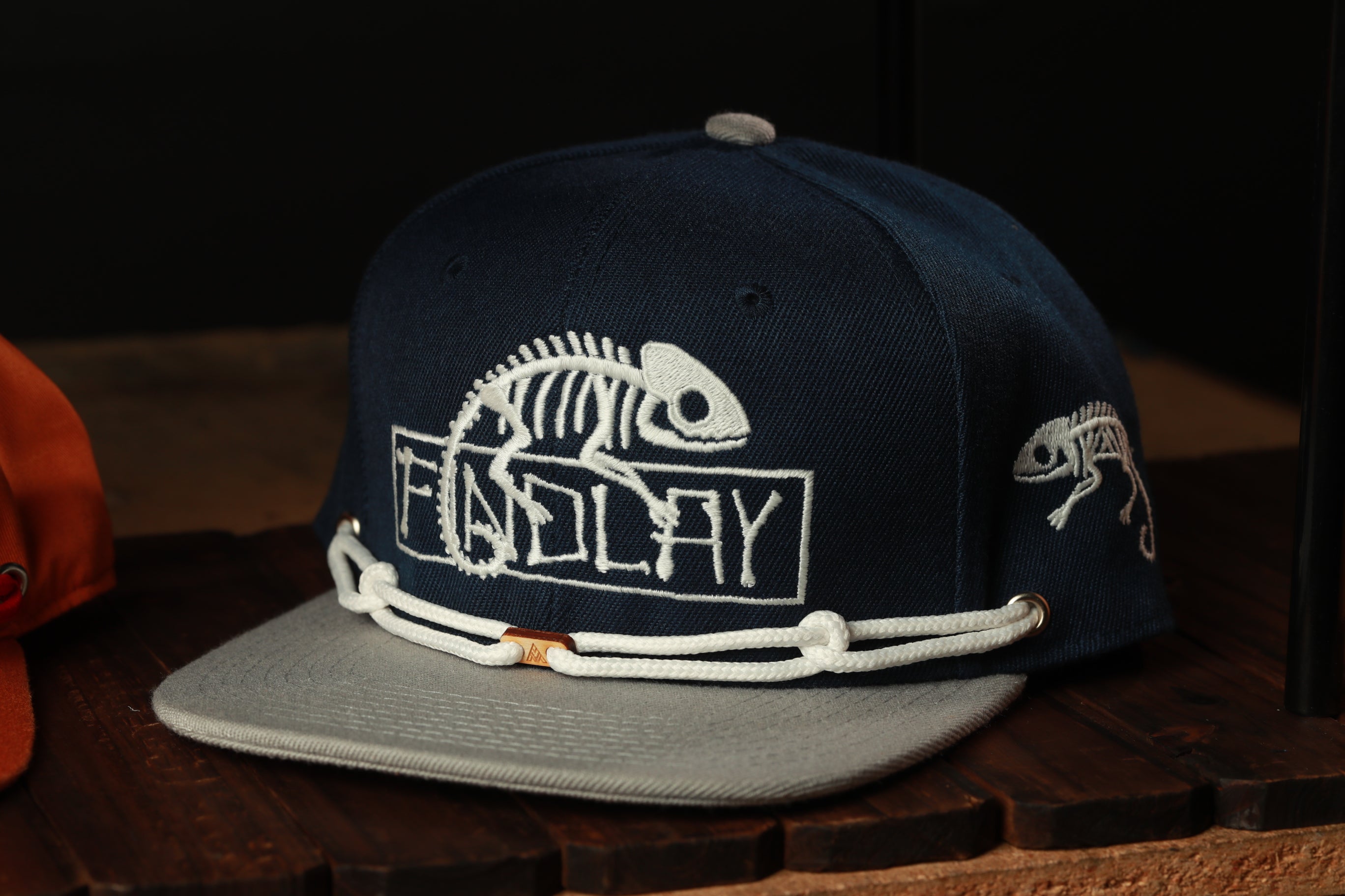 A navy blue baseball cap with white text and a chameleon design, displayed on a wooden surface.