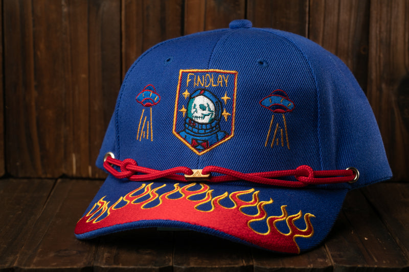 A blue baseball cap with a red and yellow flame design, featuring a skull and a rocket ship on the front.
