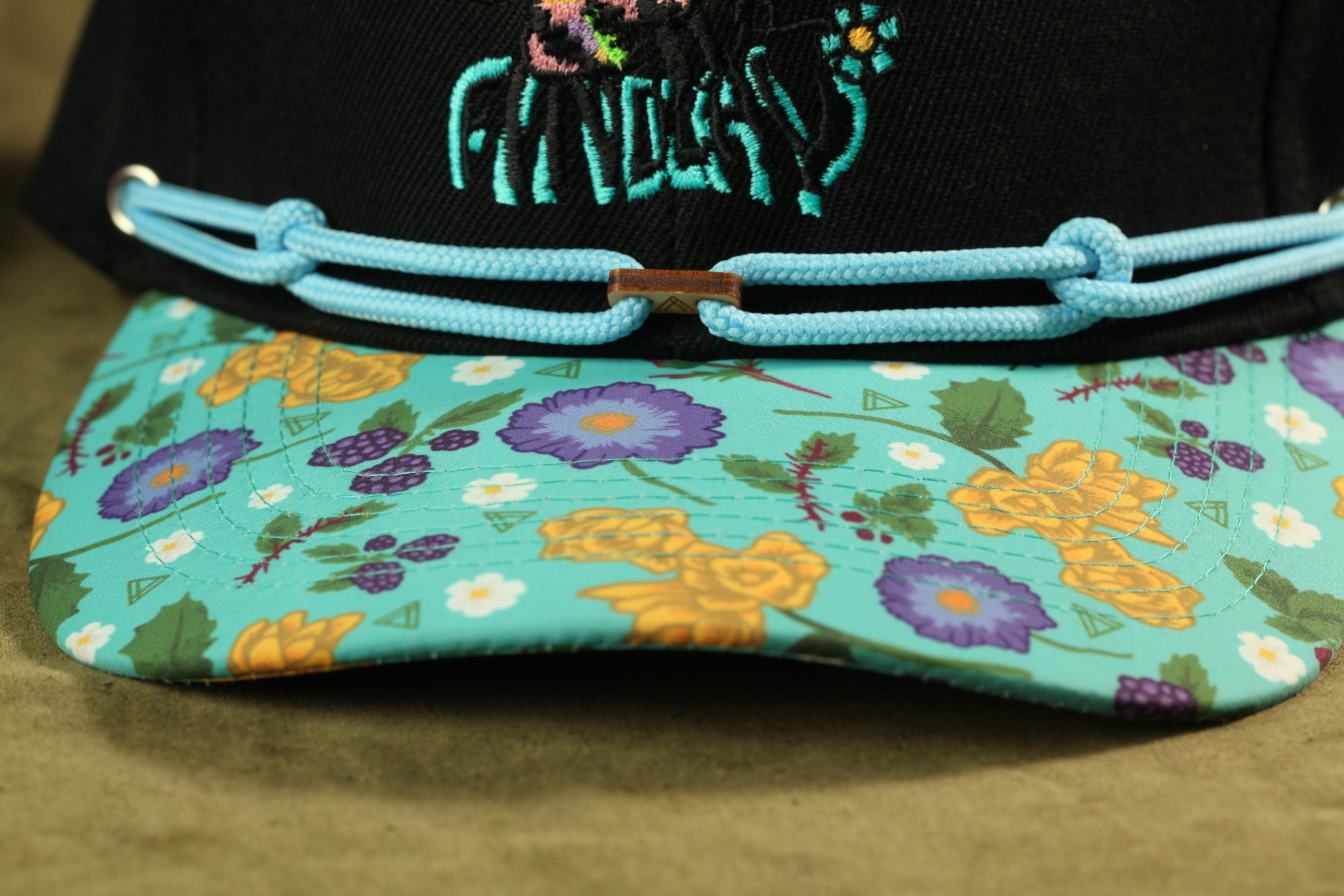 A close-up view of a colorful floral pattern on a baseball cap, with a black brim and blue straps.