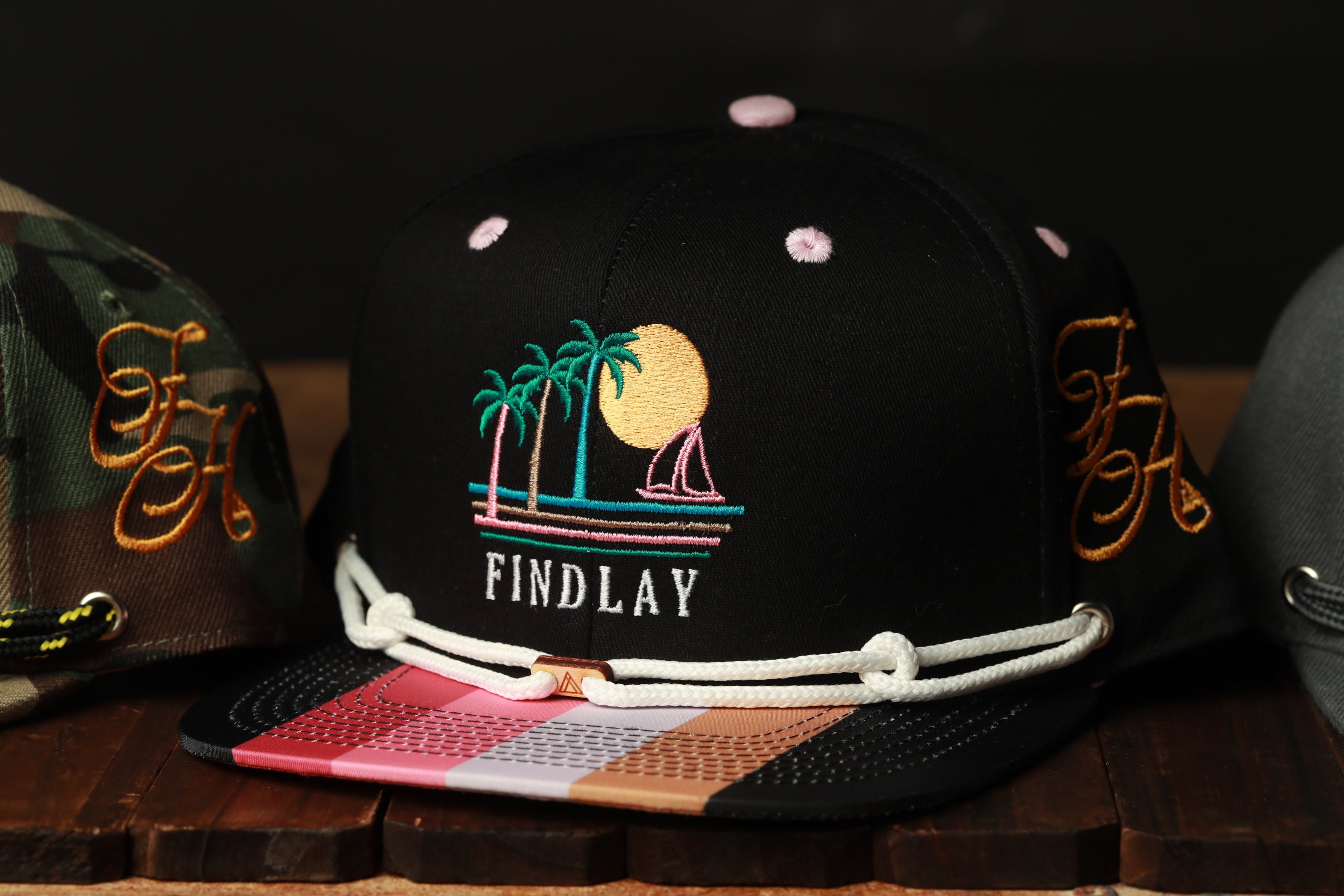 A black baseball cap with a colorful graphic and text on it, displayed on a wooden surface.