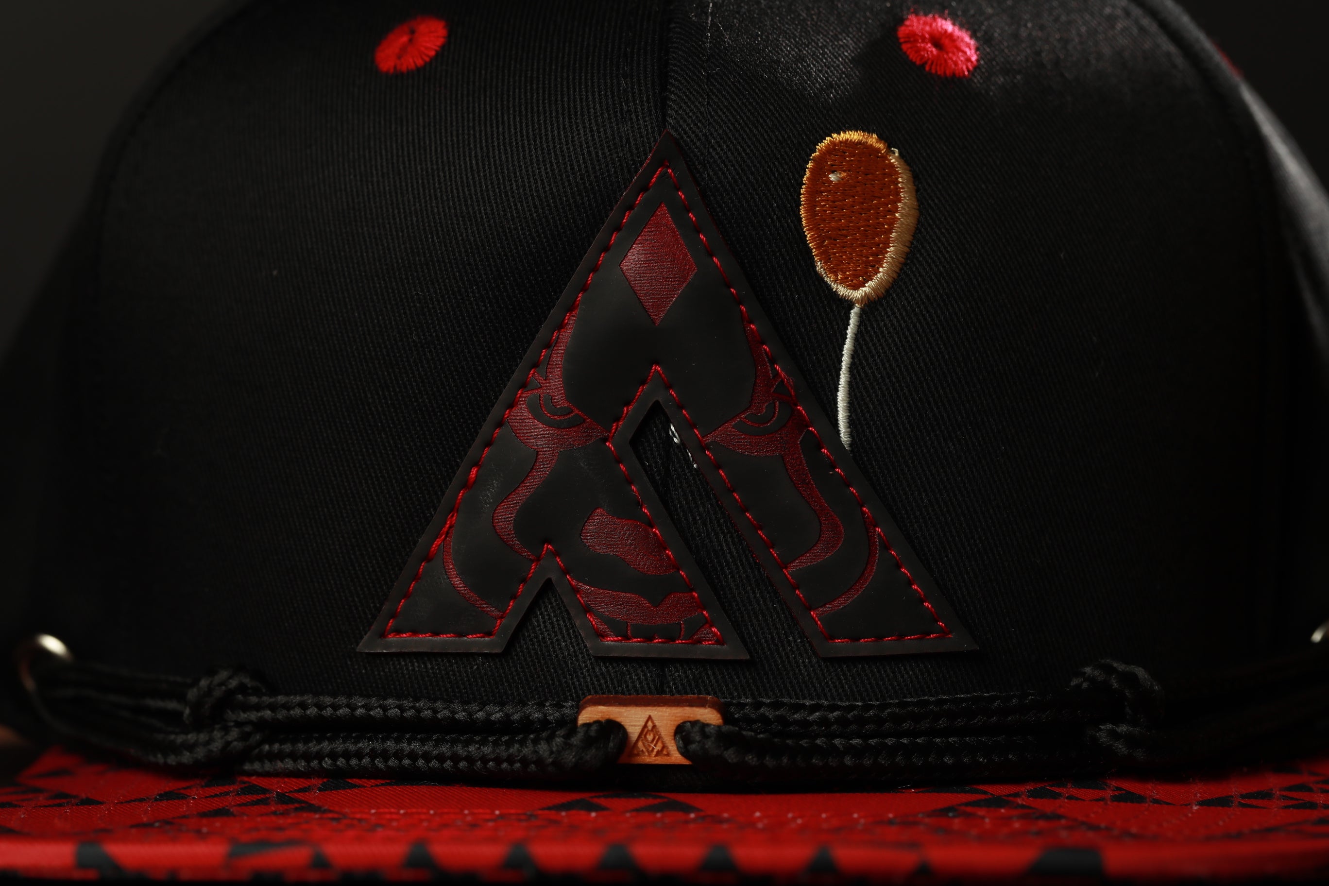 A close-up view of a black baseball cap with a red and black logo on the front.