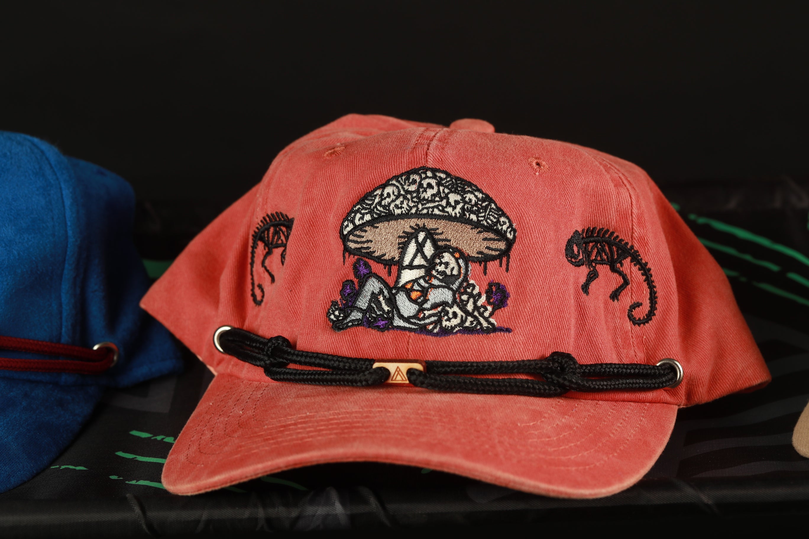 A red baseball cap with a mushroom design and a black strap is displayed on a surface.