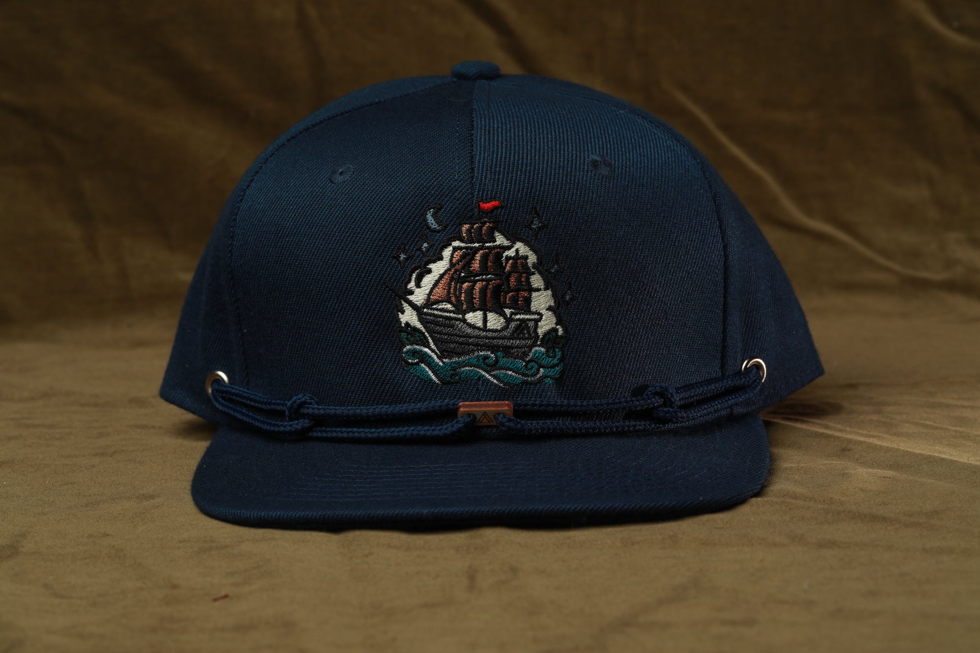 A navy blue baseball cap with a ship embroidered on the front.