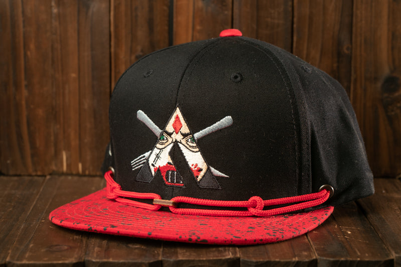 A black baseball cap with a red brim and a red and white embroidered logo on the front, sitting on a wooden surface.